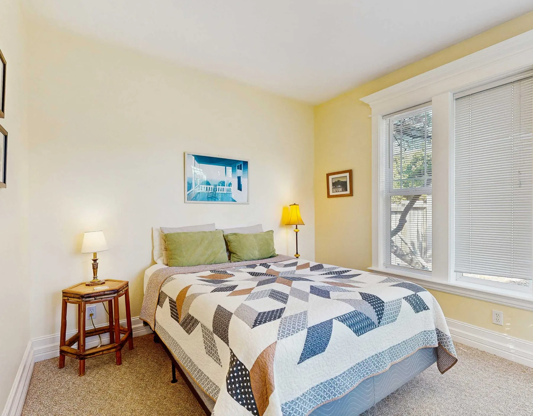 Dormitorio con una cama bajo un cuadro y ventanas con persianas.