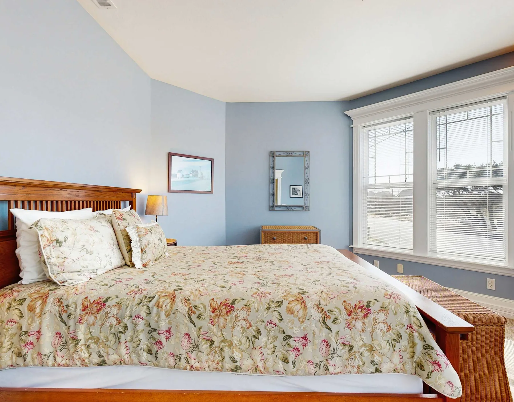 Un dormitorio con una colcha floral y ventanas grandes.