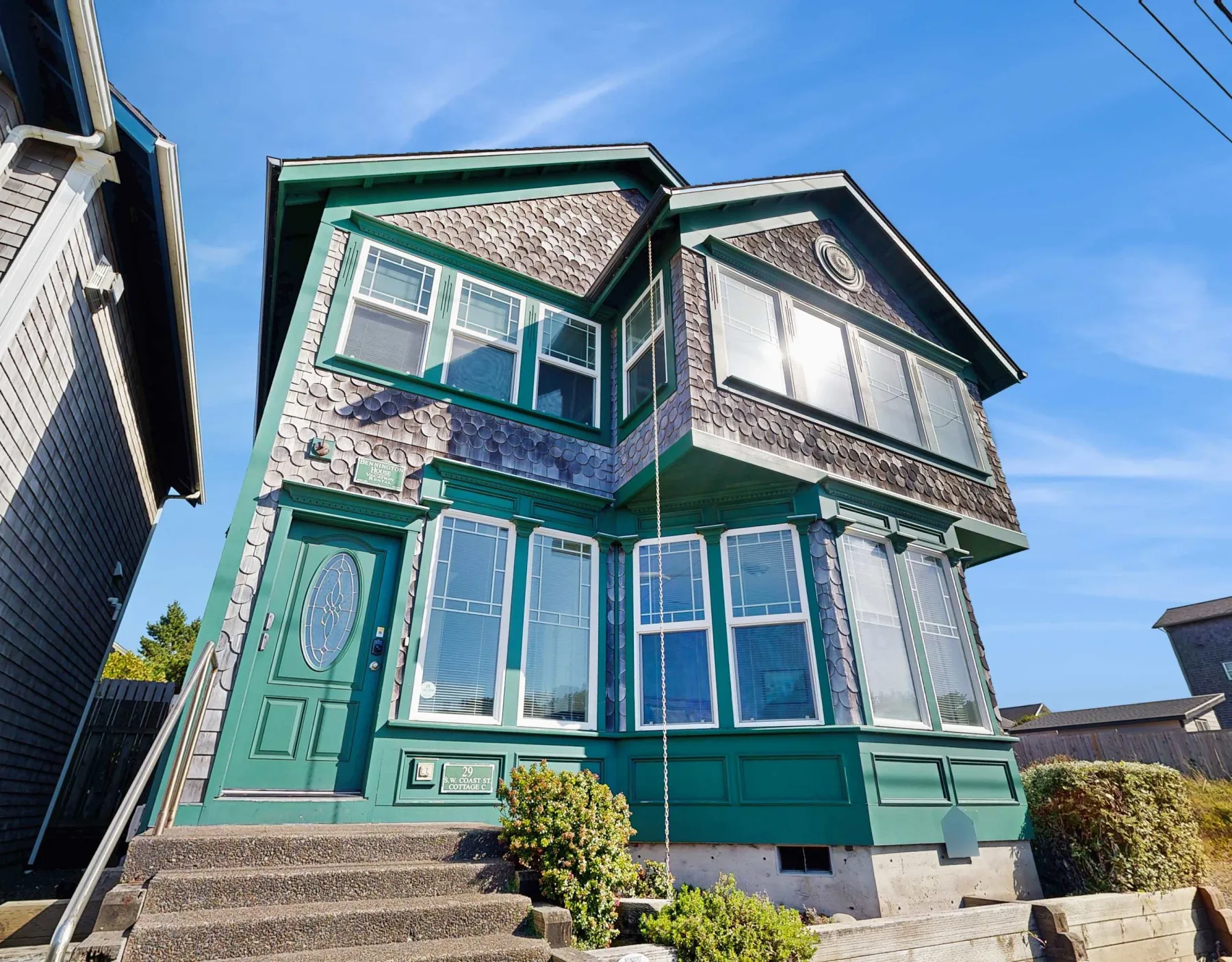 Una casa verde azulado de dos pisos con ventanas grandes y entrada principal.