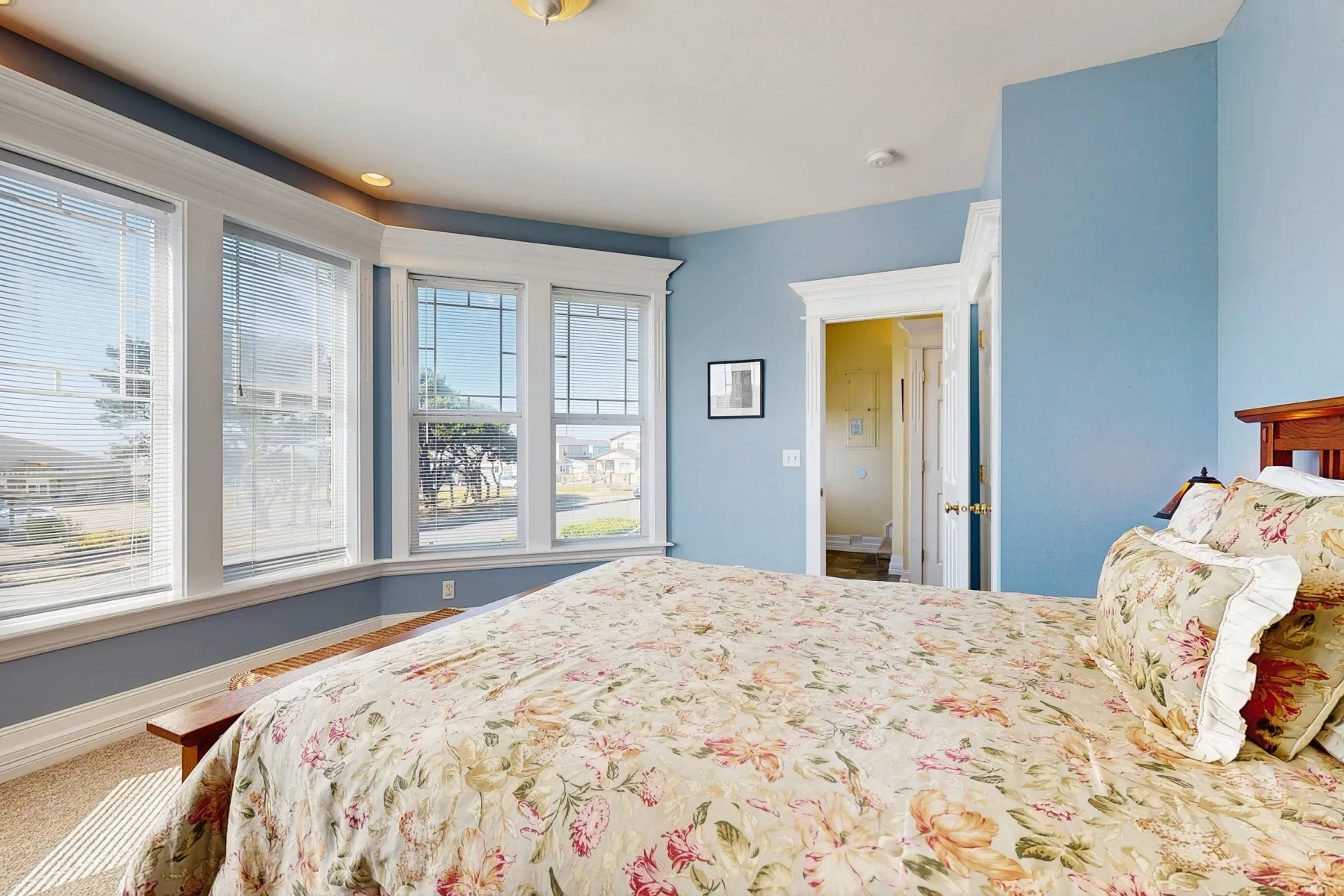 Un dormitorio con una colcha floral y grandes ventanas.