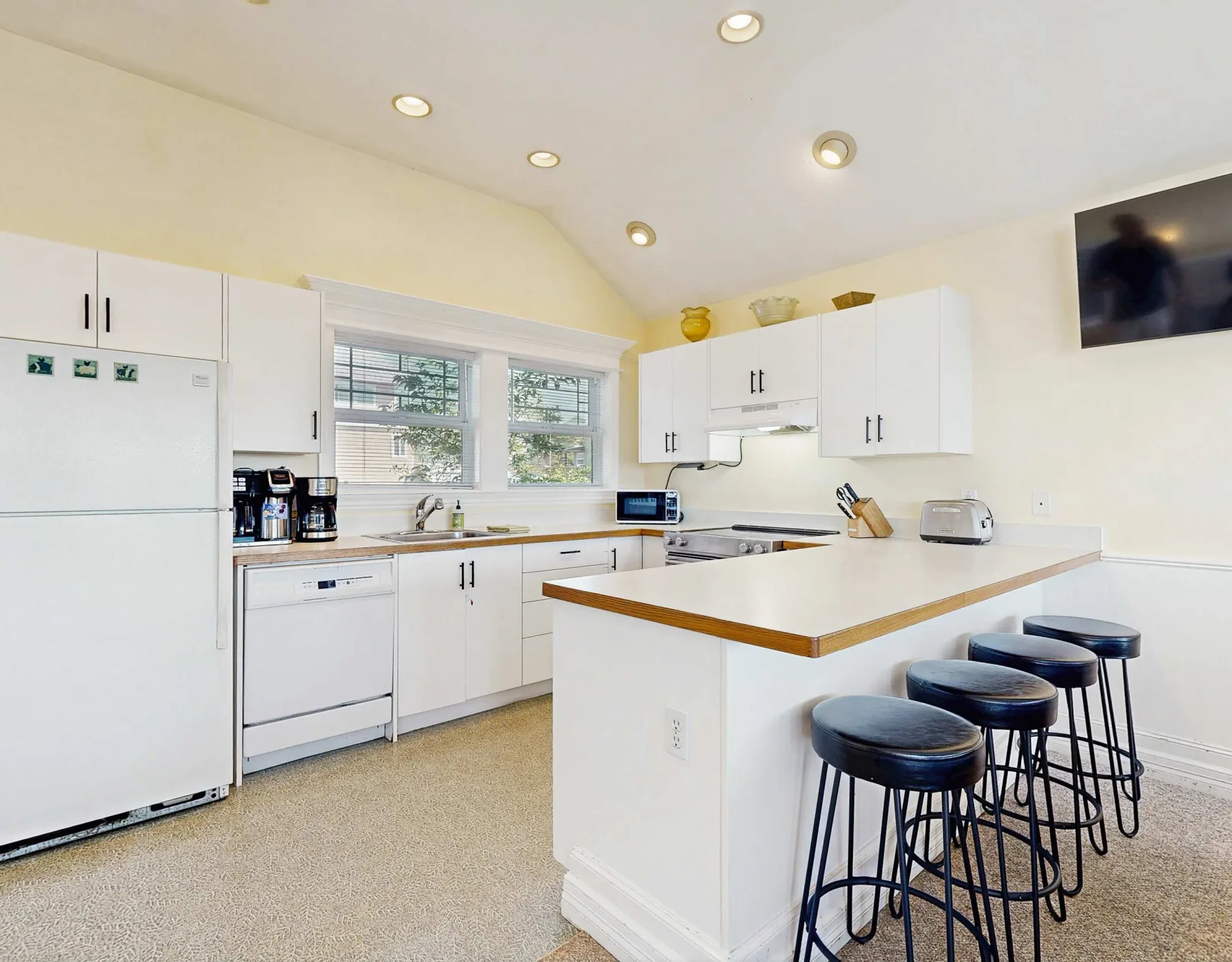 Una cocina luminosa con gabinetes blancos y una barra con asientos.