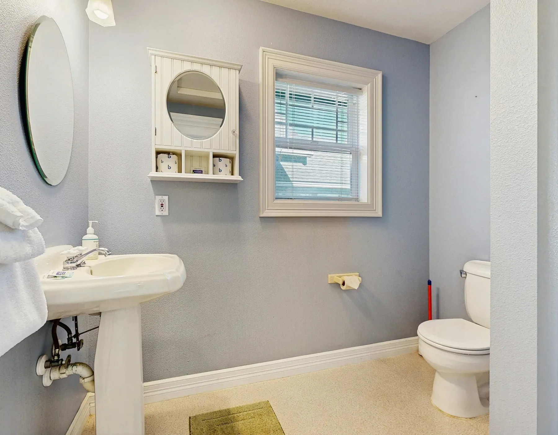 Un baño con lavabo de pedestal, ventana e inodoro.