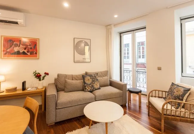 A bright living room with a sofa, seating, and windows overlooking nearby buildings.