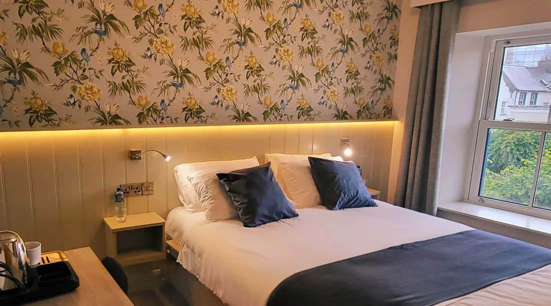Representative hotel space: A bedroom with a neatly made bed beneath floral wallpaper.