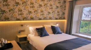 Representative hotel space: A bedroom with a double bed, dark pillows, and floral wallpaper.