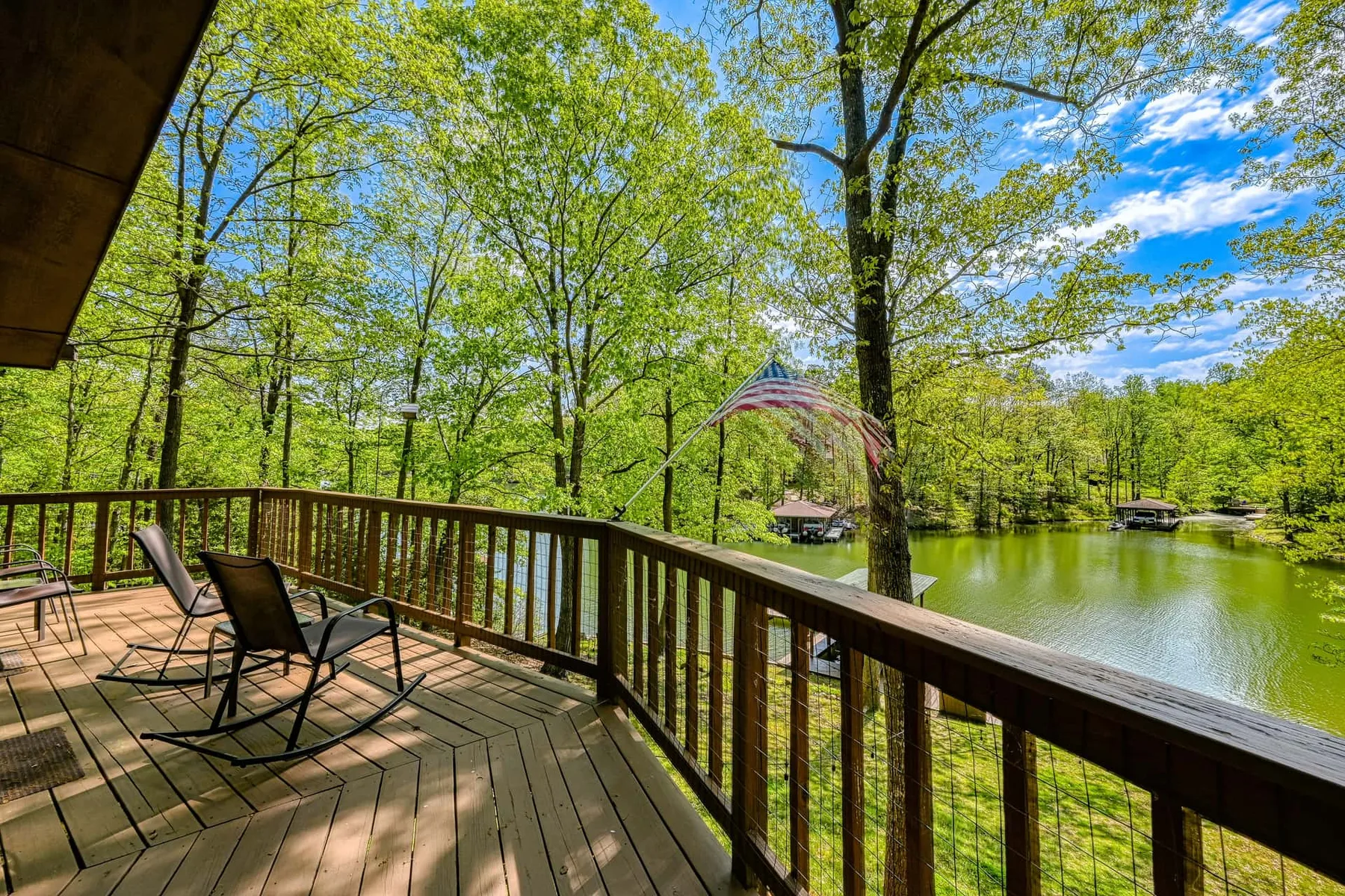 Una terraza de madera da a un lago, con asientos al aire libre bajo árboles frondosos.