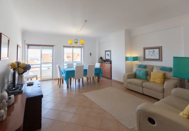 A bright living and dining room with a table, seating, and large windows.