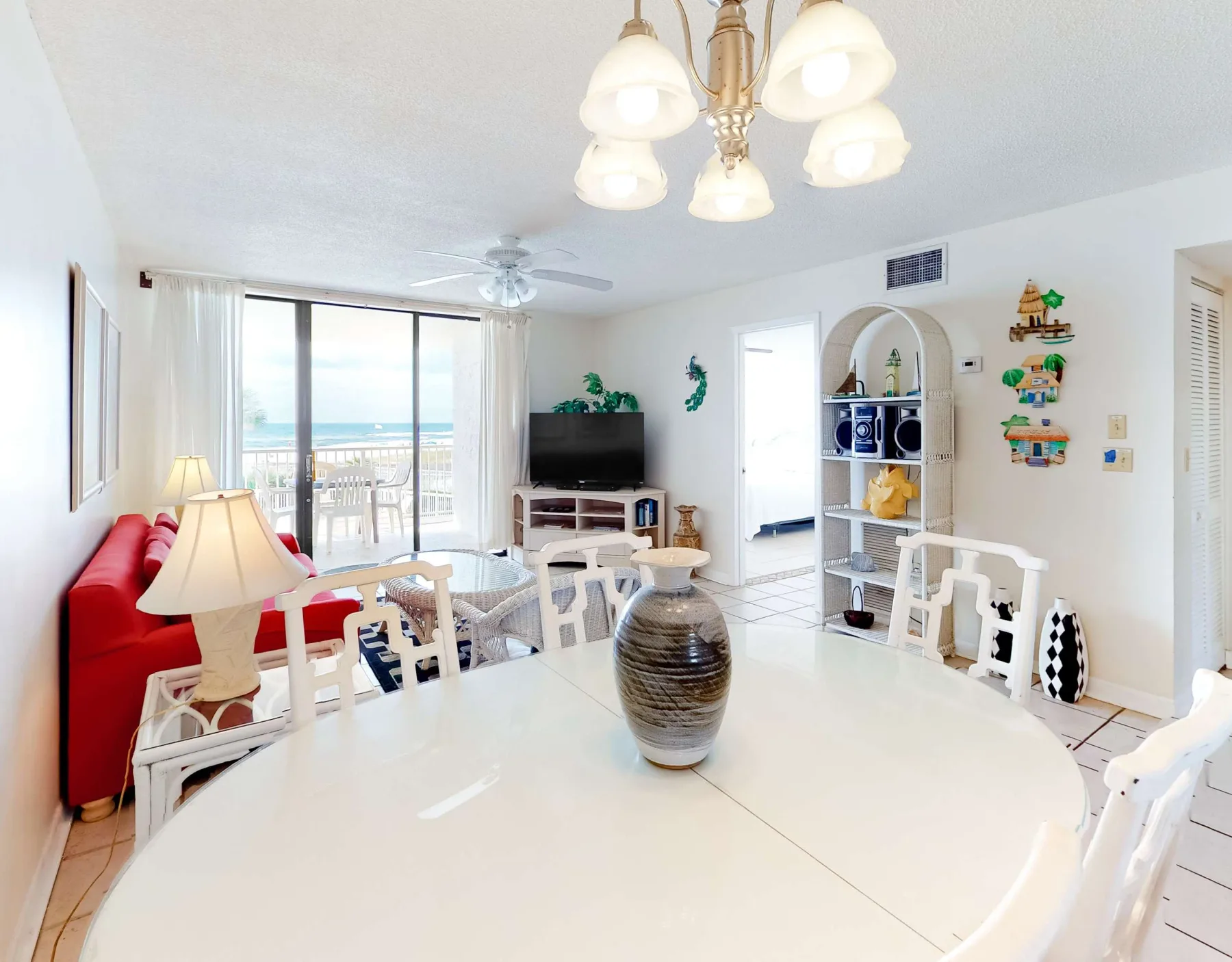 Una luminosa zona de comedor y estar tiene una mesa grande, asientos blancos y vistas al mar.