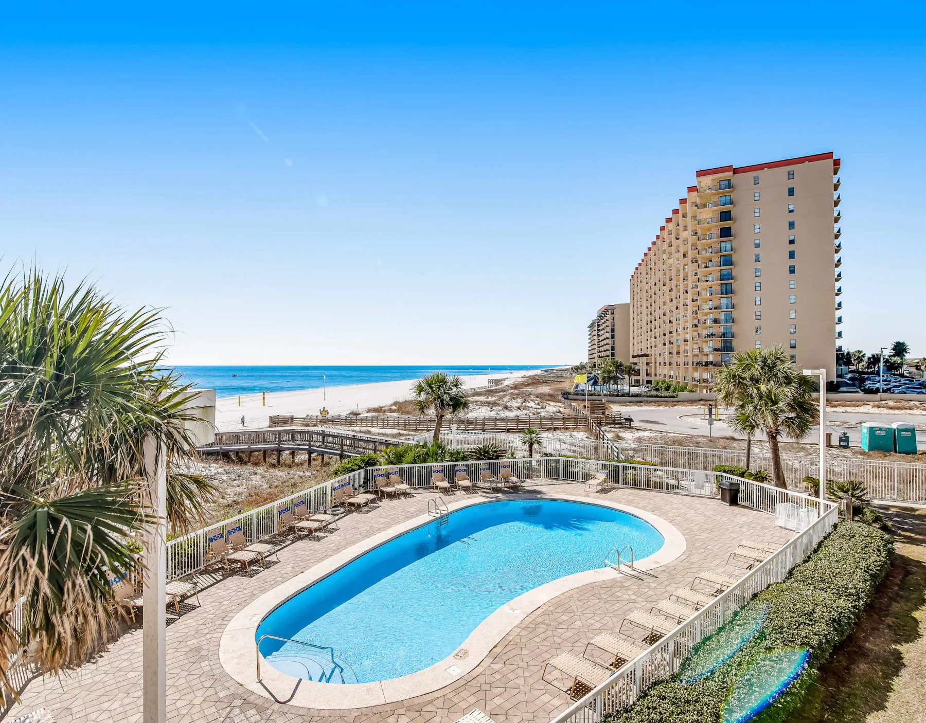 Zona común: Una piscina al aire libre está junto a una playa de arena y un edificio alto.