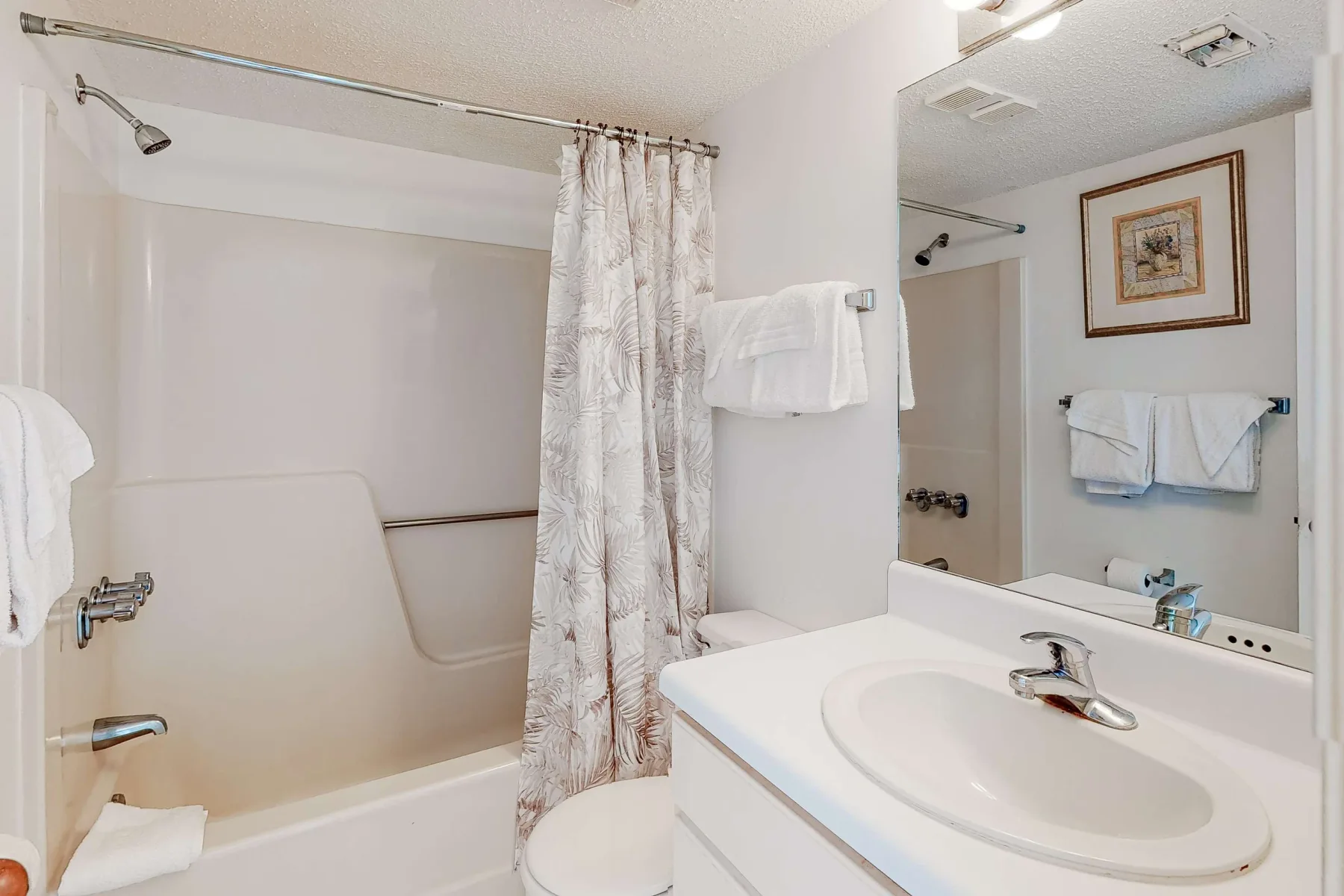 Un baño con bañera, cortina de ducha estampada y lavabo junto a un espejo grande.