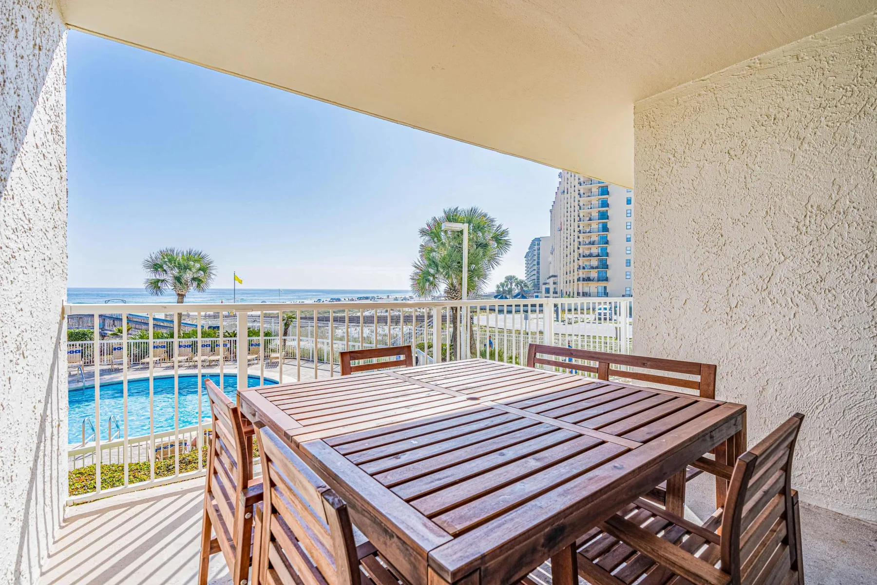 Un balcón cubierto tiene una mesa de comedor de madera y vista al mar.