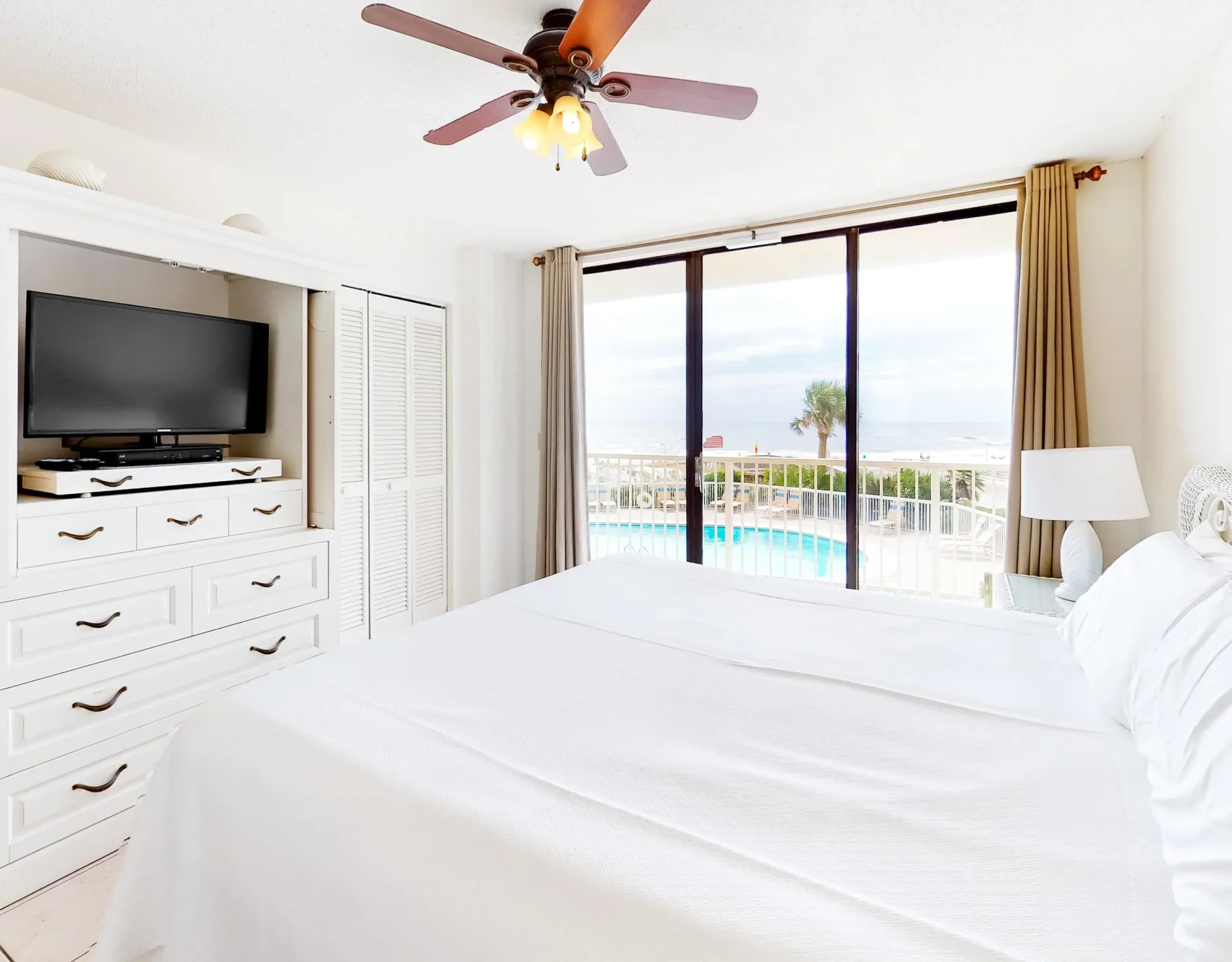 Un dormitorio luminoso con ropa de cama blanca y puertas corredizas con vistas a una piscina.