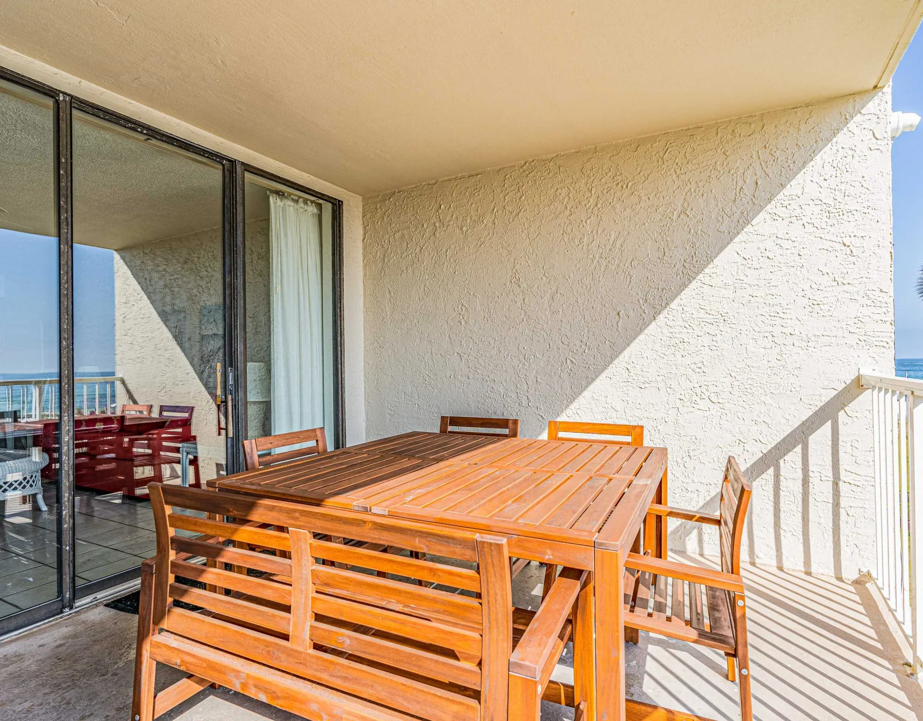 Un comedor en un balcón con mesa de madera y asientos junto a puertas corredizas de vidrio.