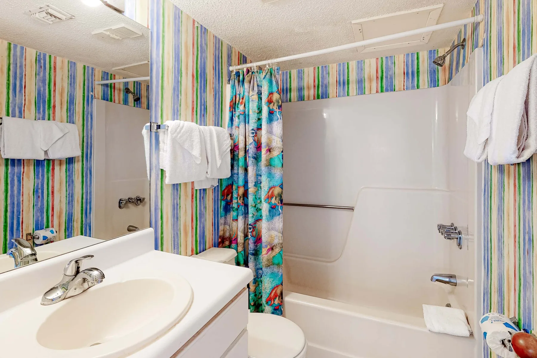 Un baño con lavabo, inodoro y bañera detrás de una cortina de ducha colorida.
