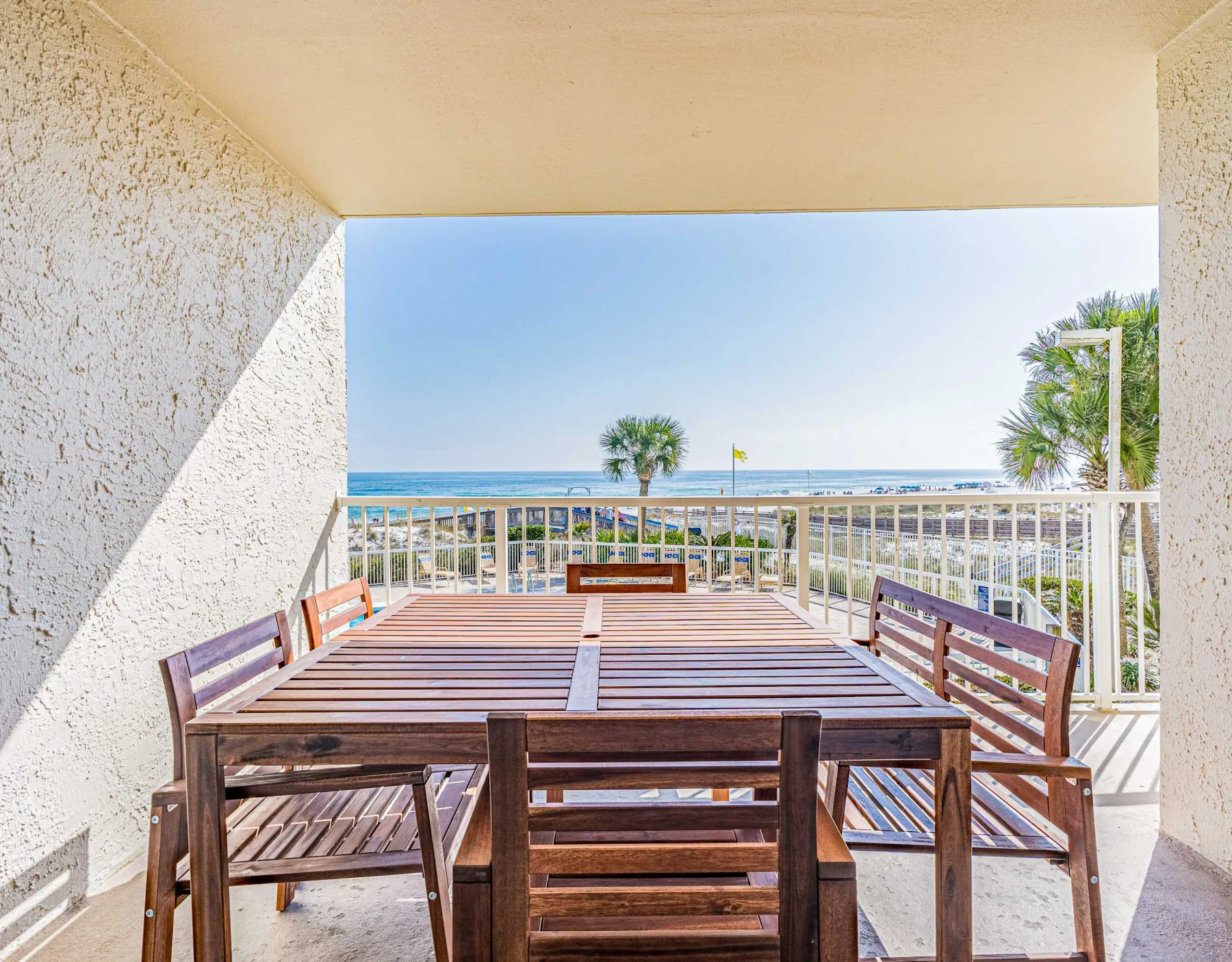 Asientos en un patio cubierto con vistas al océano tras una barandilla blanca.
