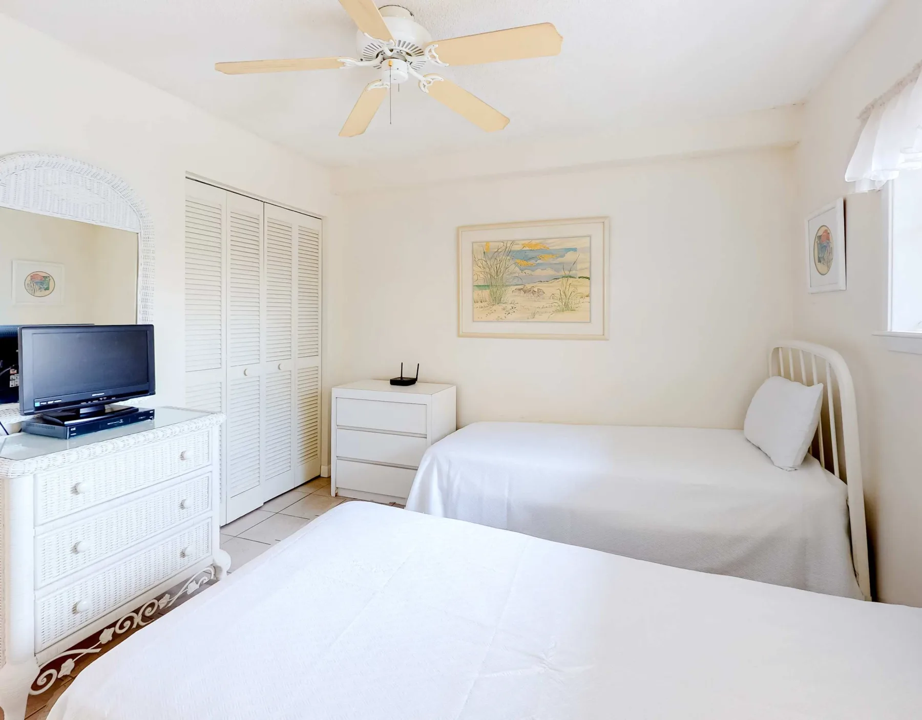 Un dormitorio luminoso con dos camas, cómodas blancas y un ventilador de techo.