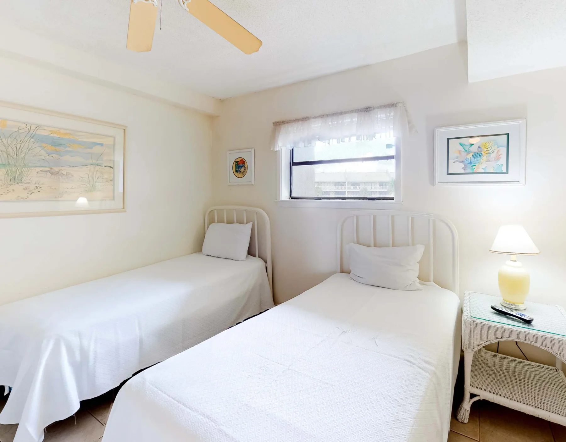 Un dormitorio luminoso con dos camas, cuadros enmarcados y una lámpara de noche.