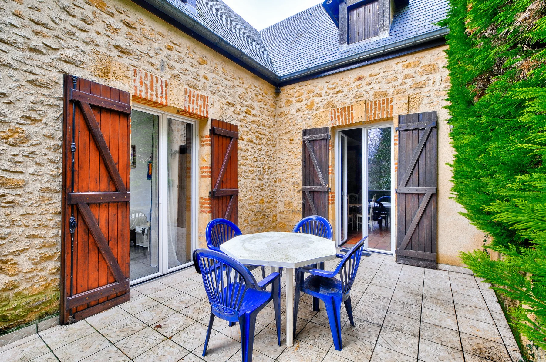 Un patio de piedra con una mesa y sillas azules está junto a puertas de vidrio.