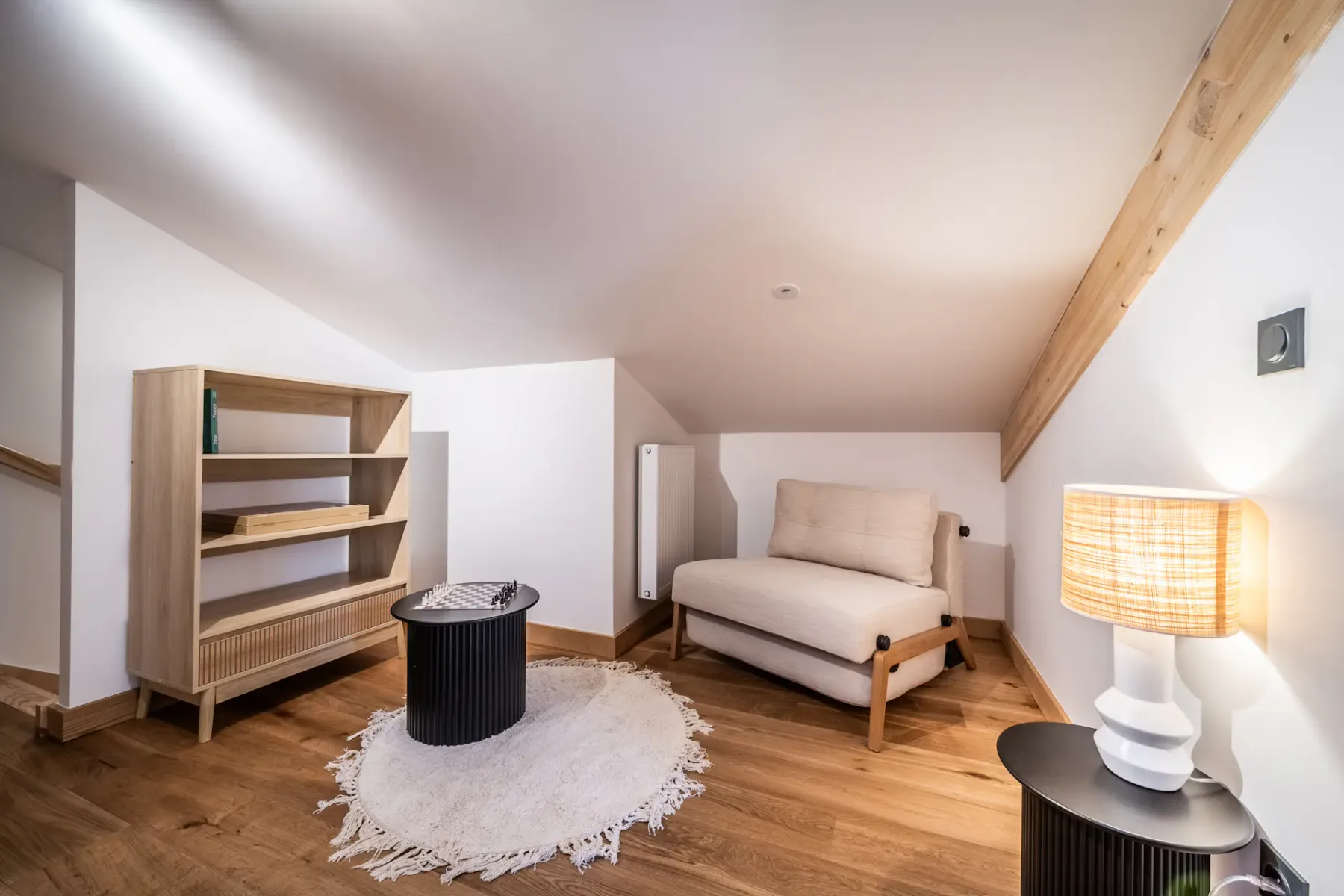 A bright attic sitting area with a low sofa, shelving, and a round coffee table.