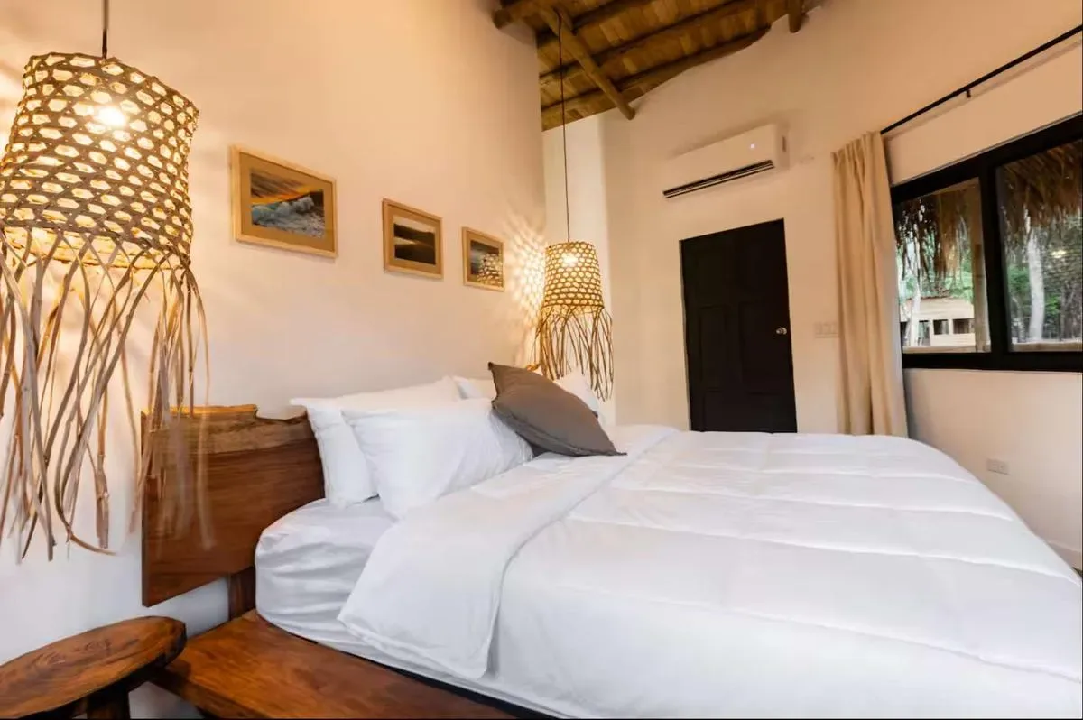 A bedroom with a white bed and woven hanging lamps.