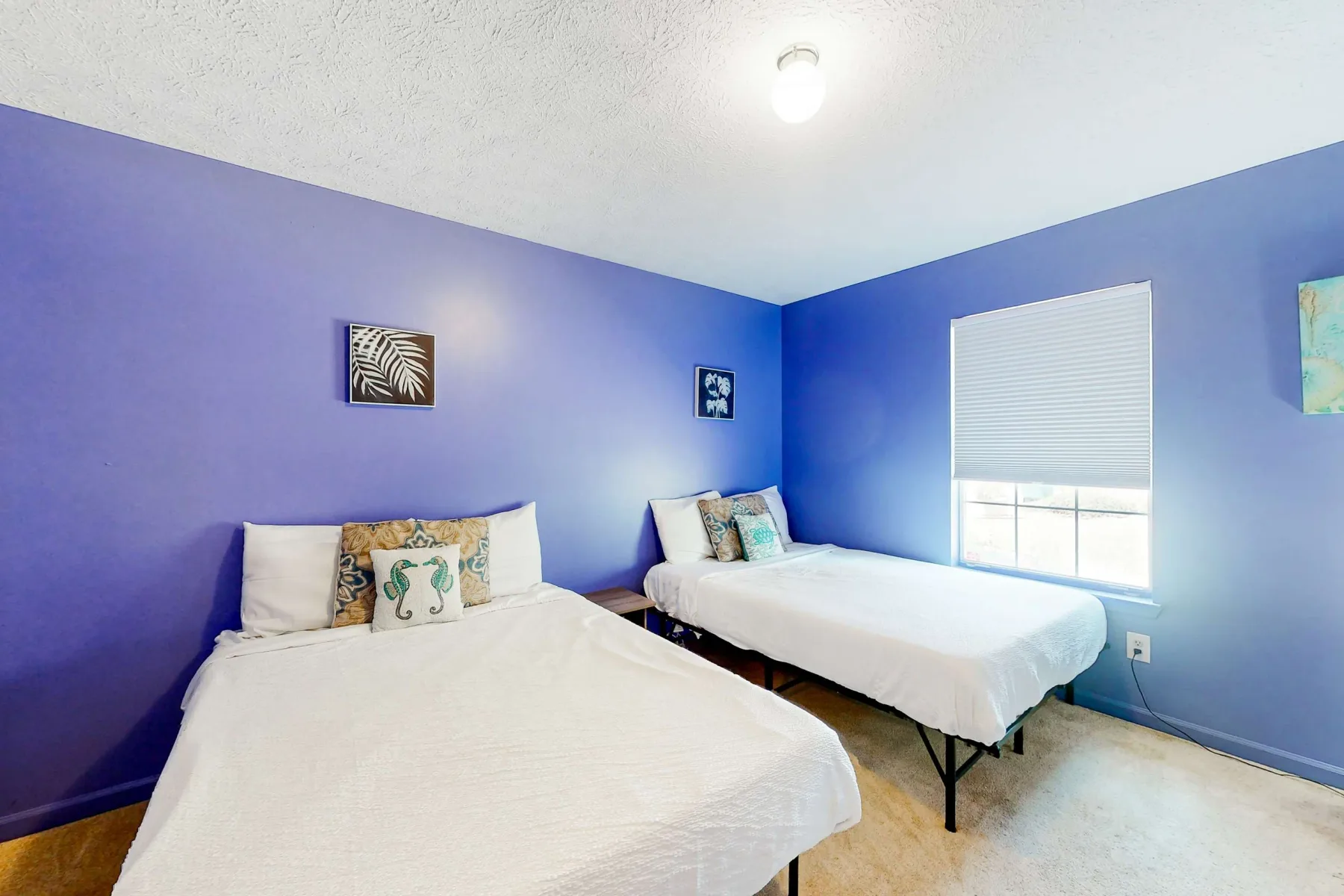 A bedroom with two beds, colorful walls, and a window with blinds.