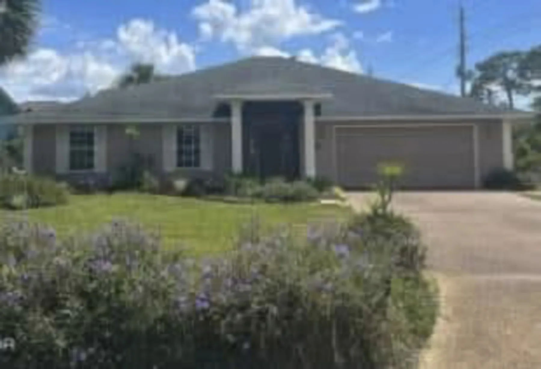 A single-story house with a front lawn and driveway beneath a partly cloudy sky.