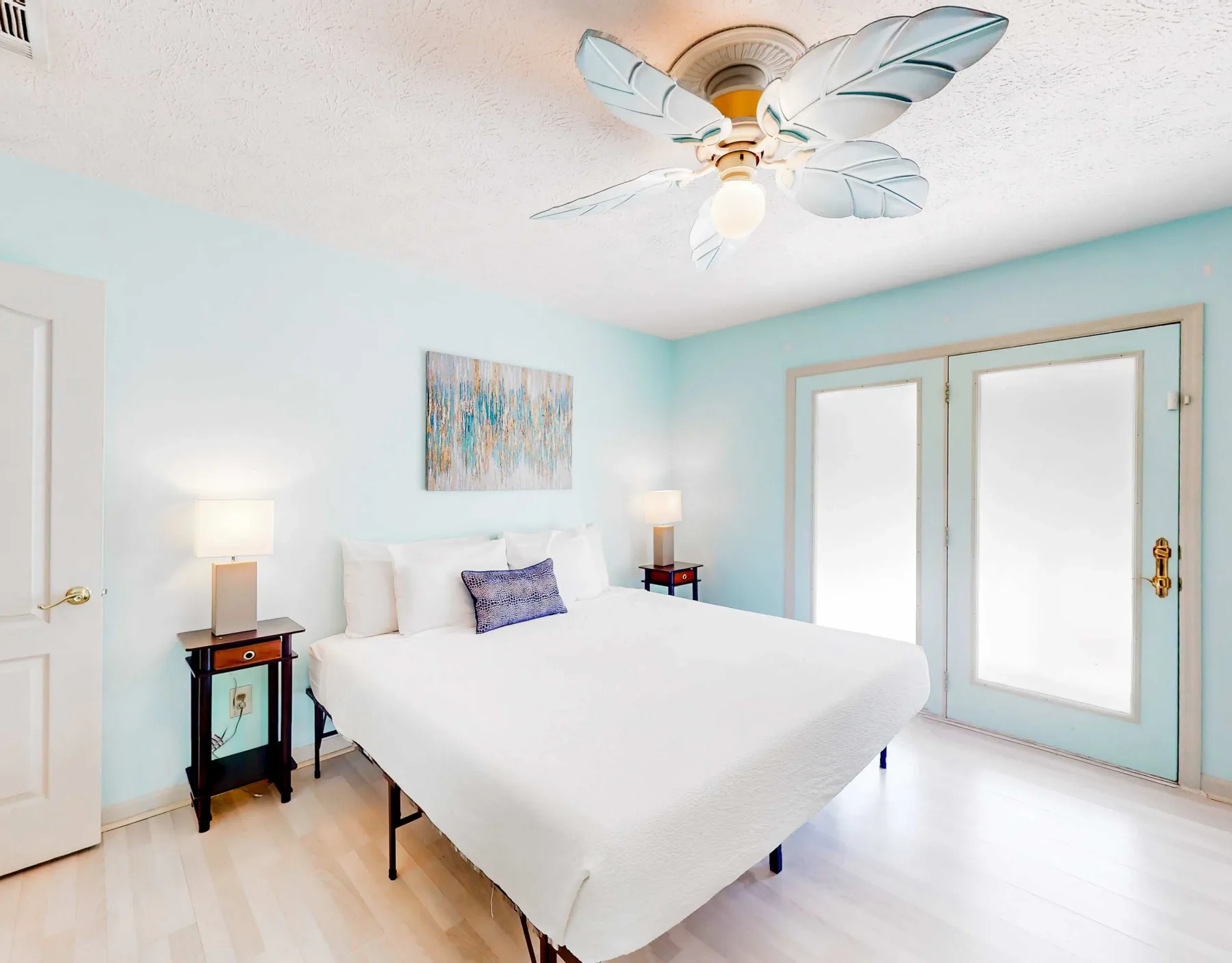 A bright bedroom with a white bed, pale blue walls, and glass doors.
