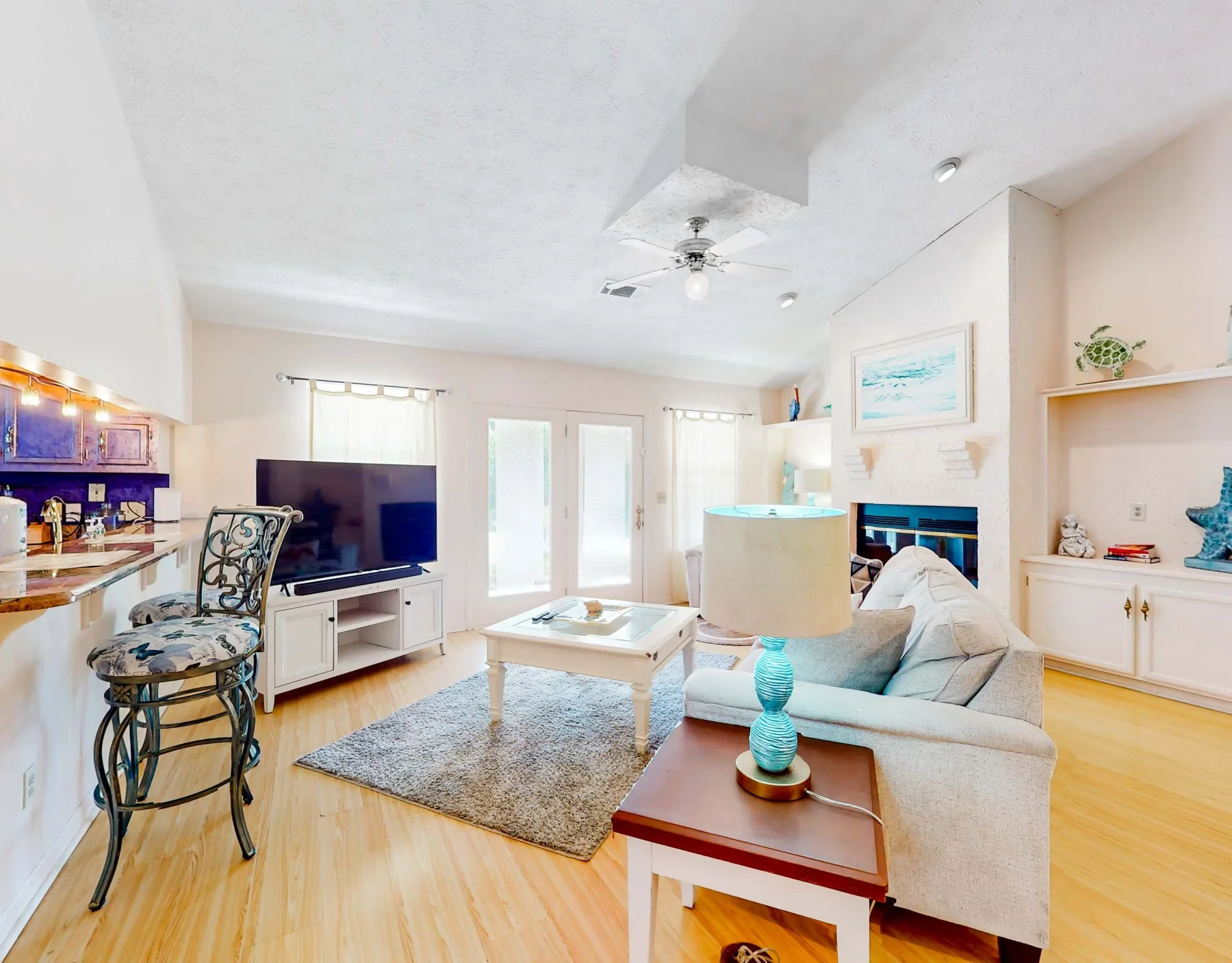 A bright living room with a seating area, television, and adjoining kitchen counter.