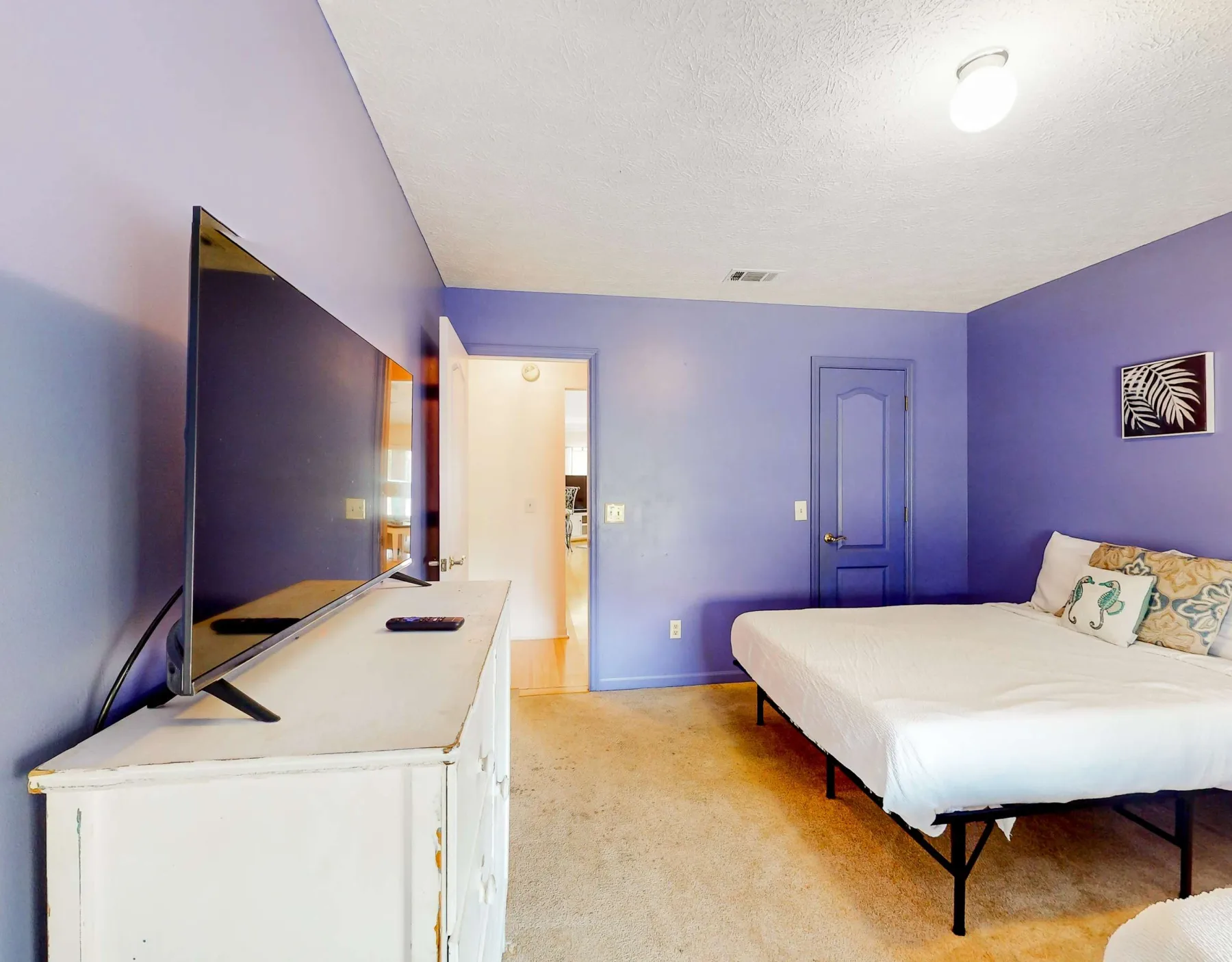 A bedroom with a bed, television, and dresser against purple walls.