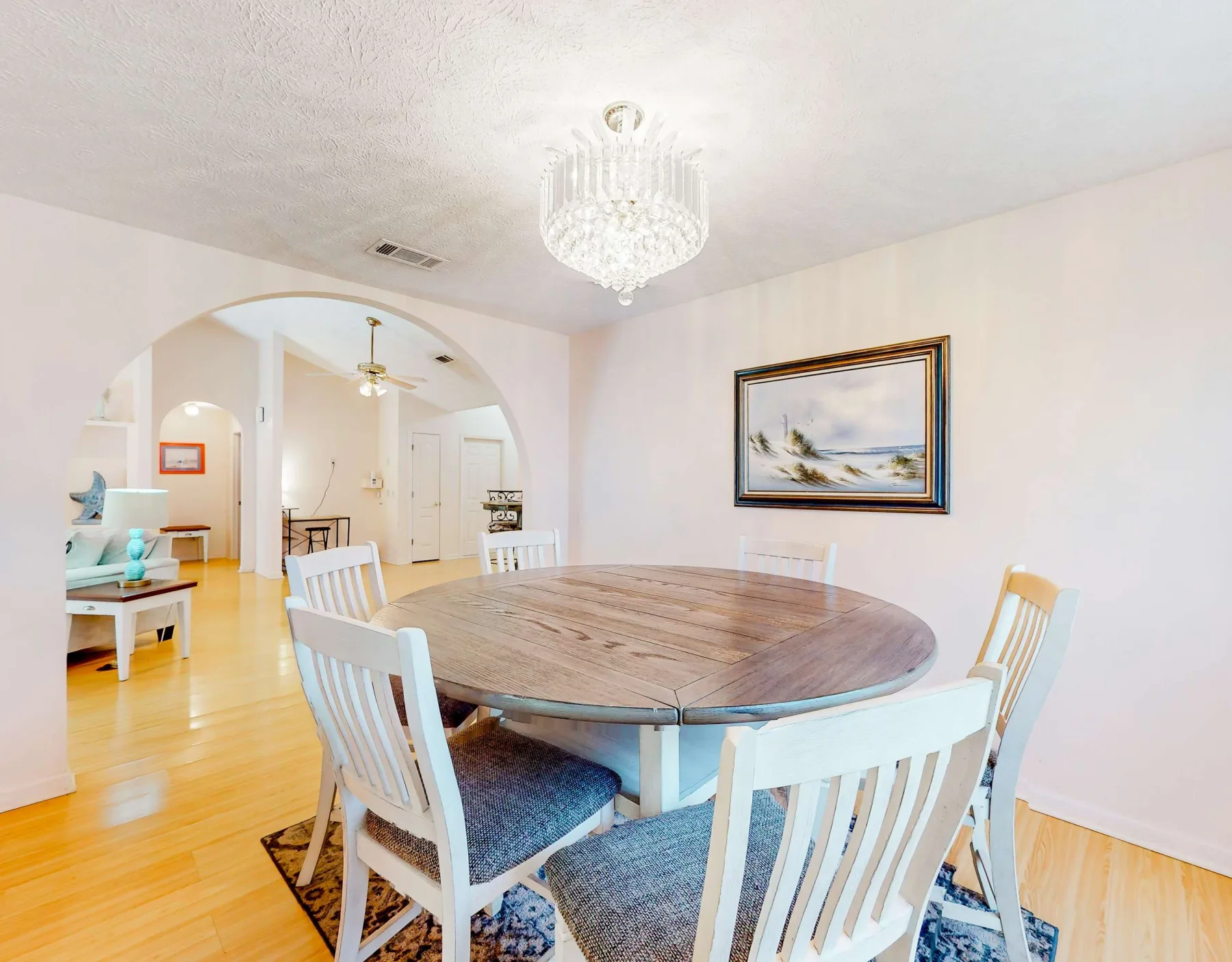 A dining area with a round wooden table, white seating, and an arched opening.