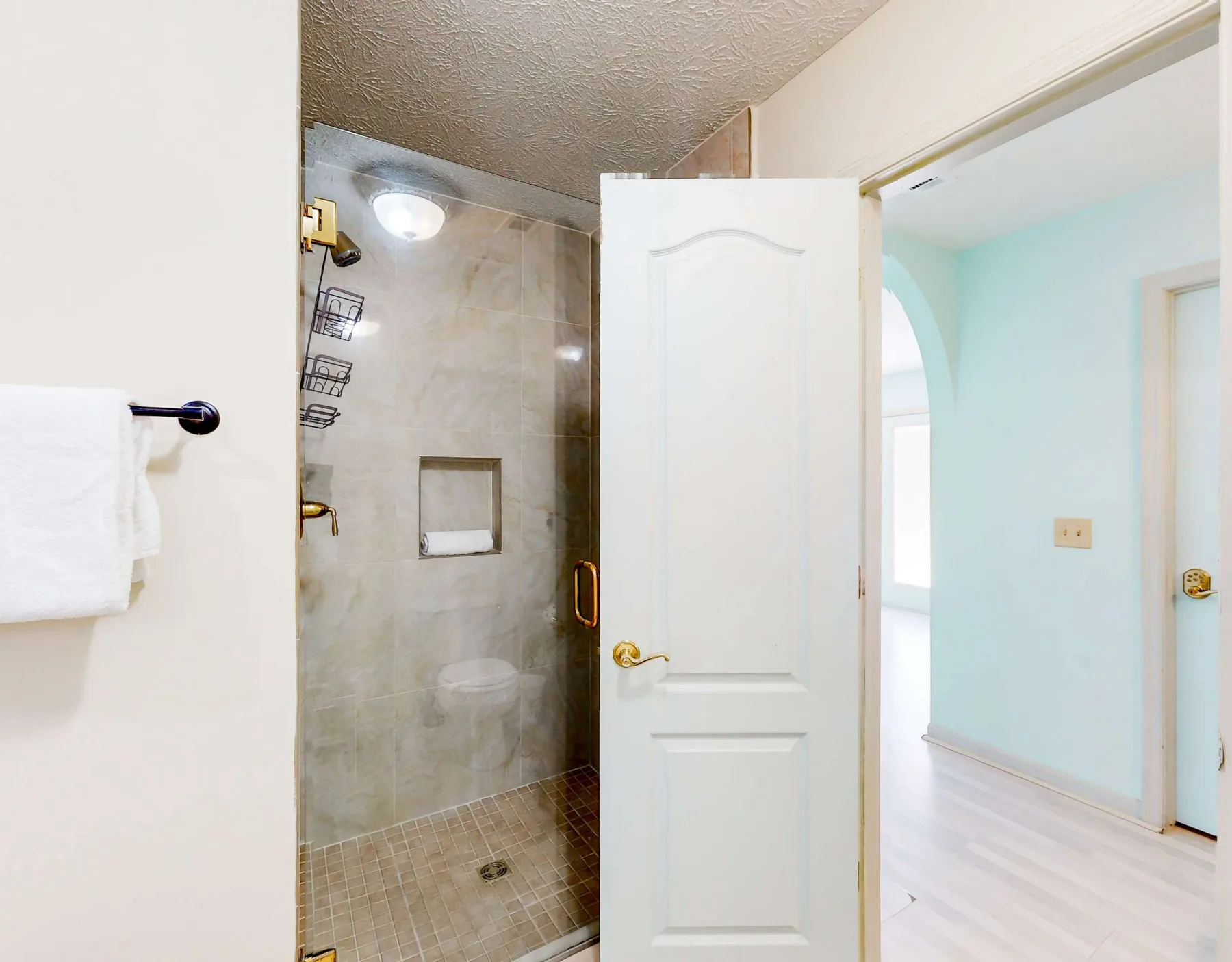 A bathroom with a tiled shower beside an open doorway.