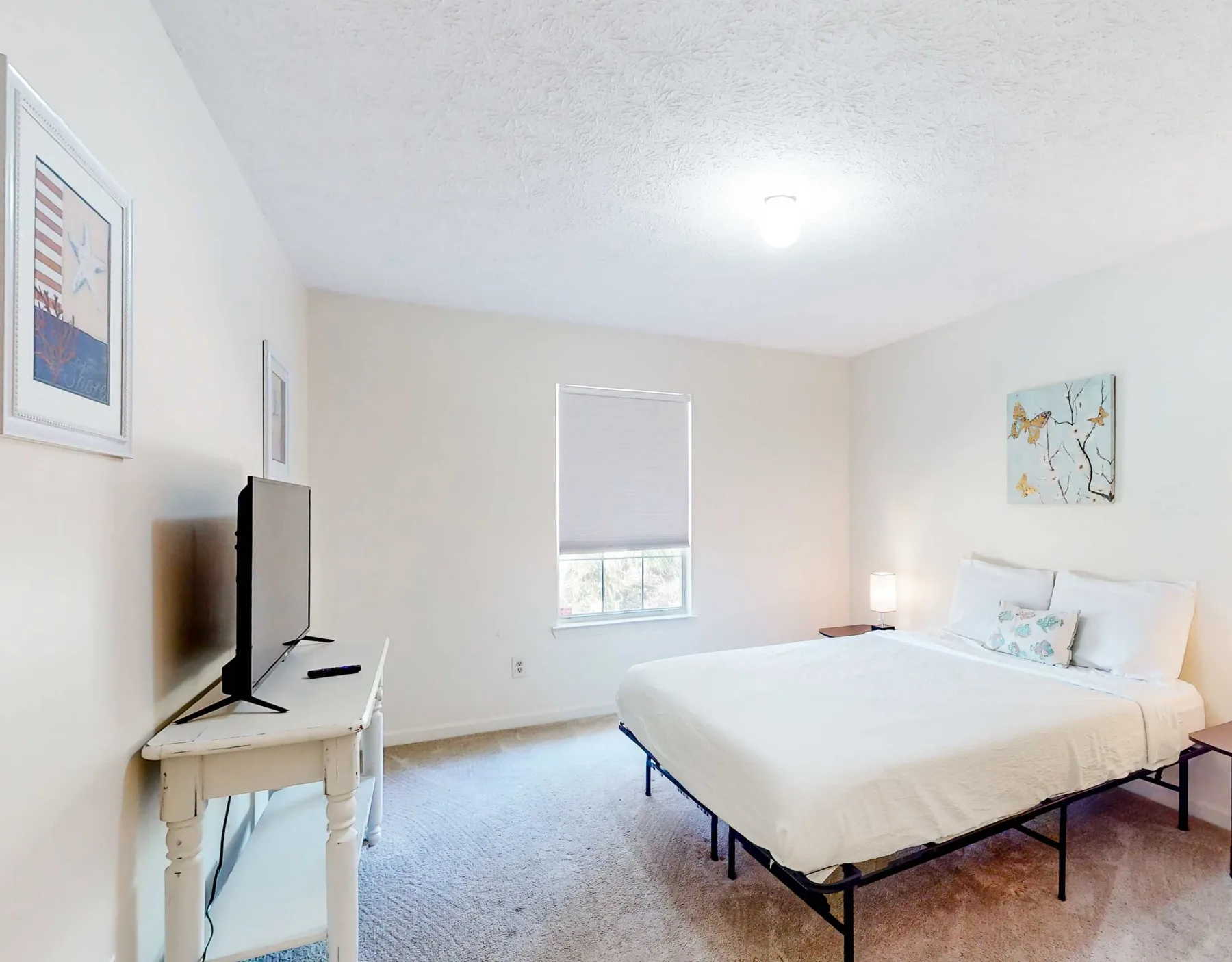 A bright bedroom with a bed, a window, and a television on a table.