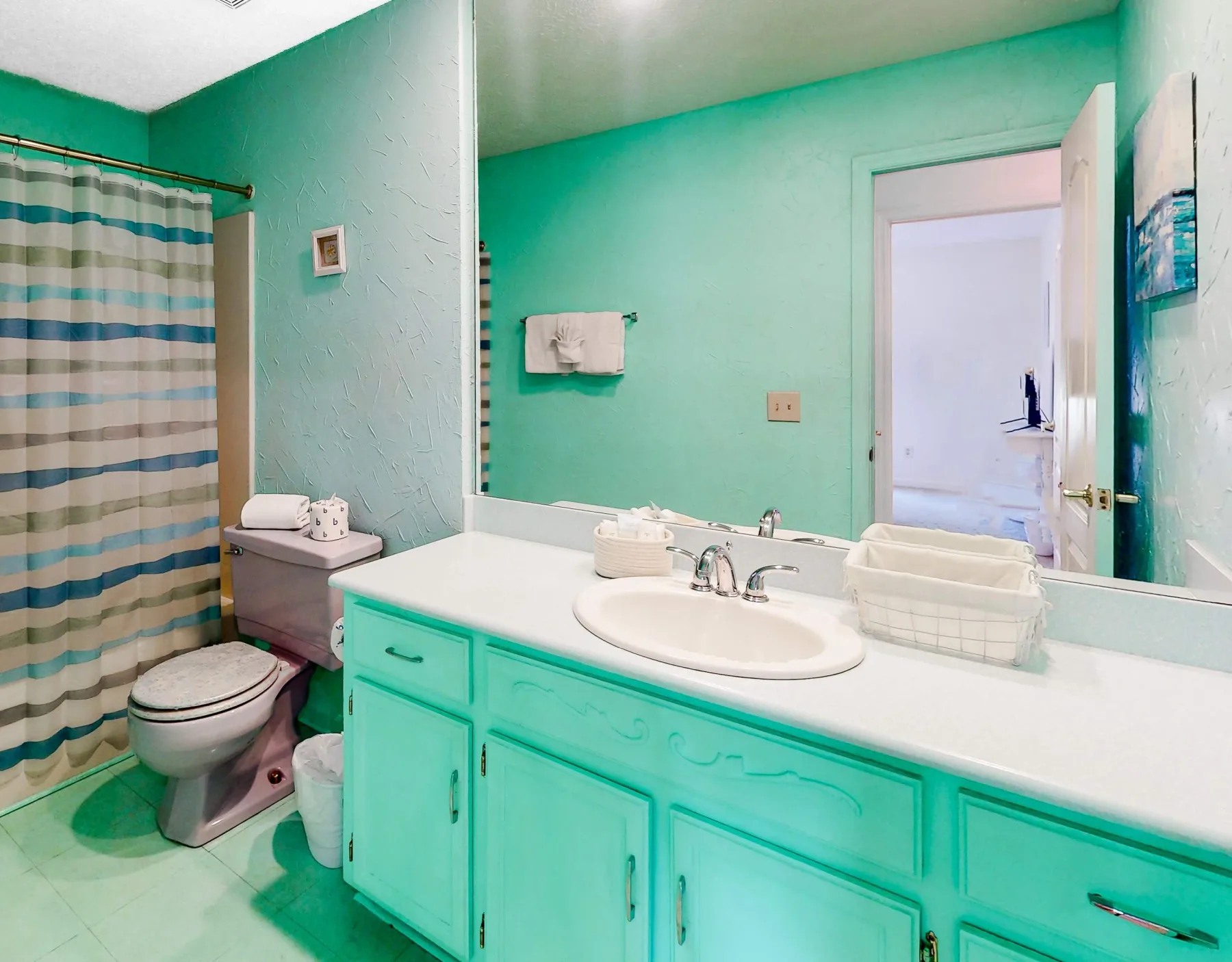A bathroom with a long vanity, sink, toilet, and striped shower curtain.