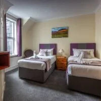 Espacio representativo del hotel: Un dormitorio con dos camas, una mesa de noche y una ventana.