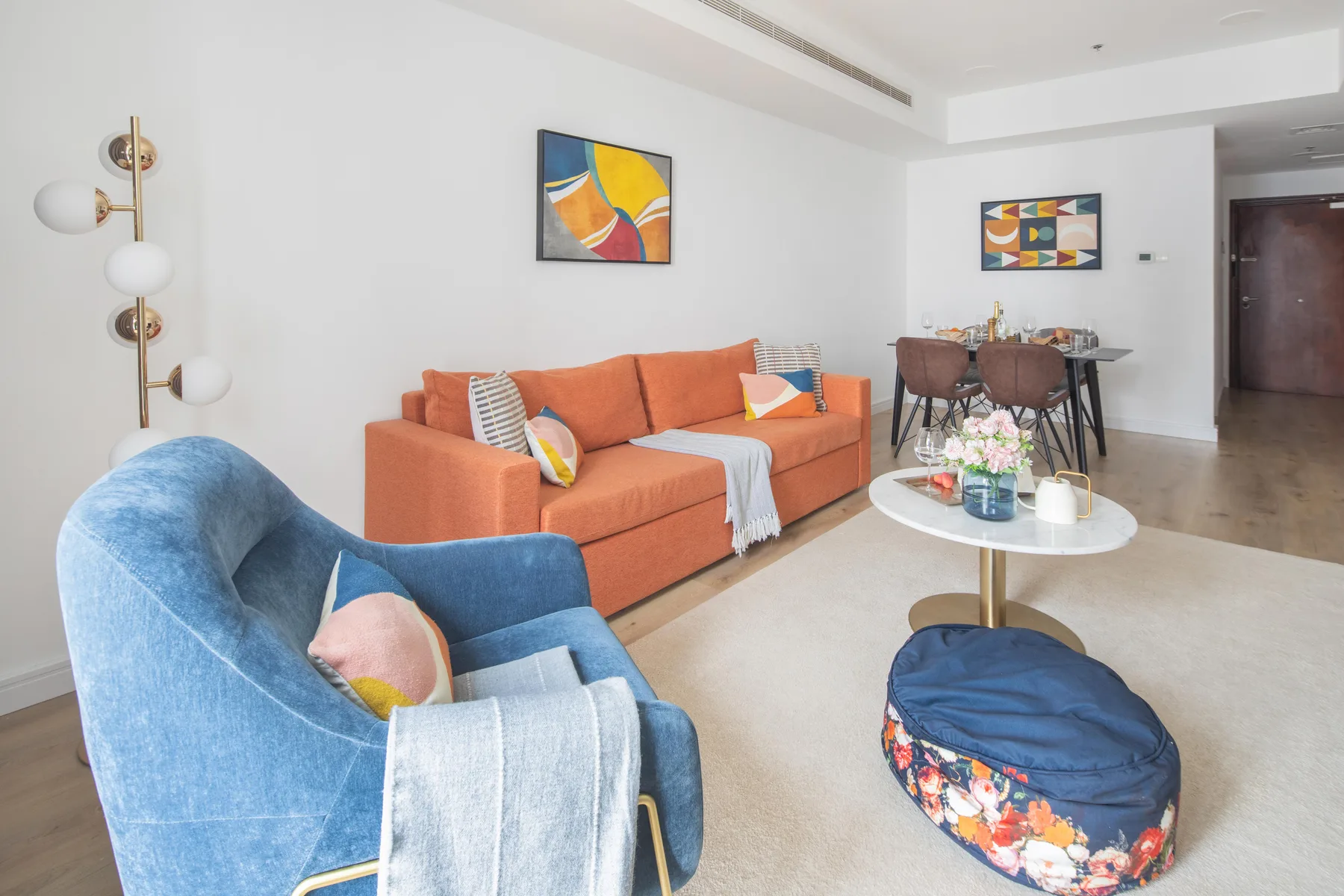 A bright living and dining area with orange seating and a table set for dining.