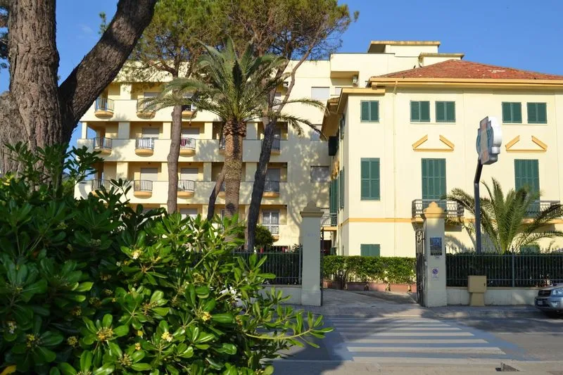 Representative hotel space: A multi-story building stands behind trees and a gated entrance.