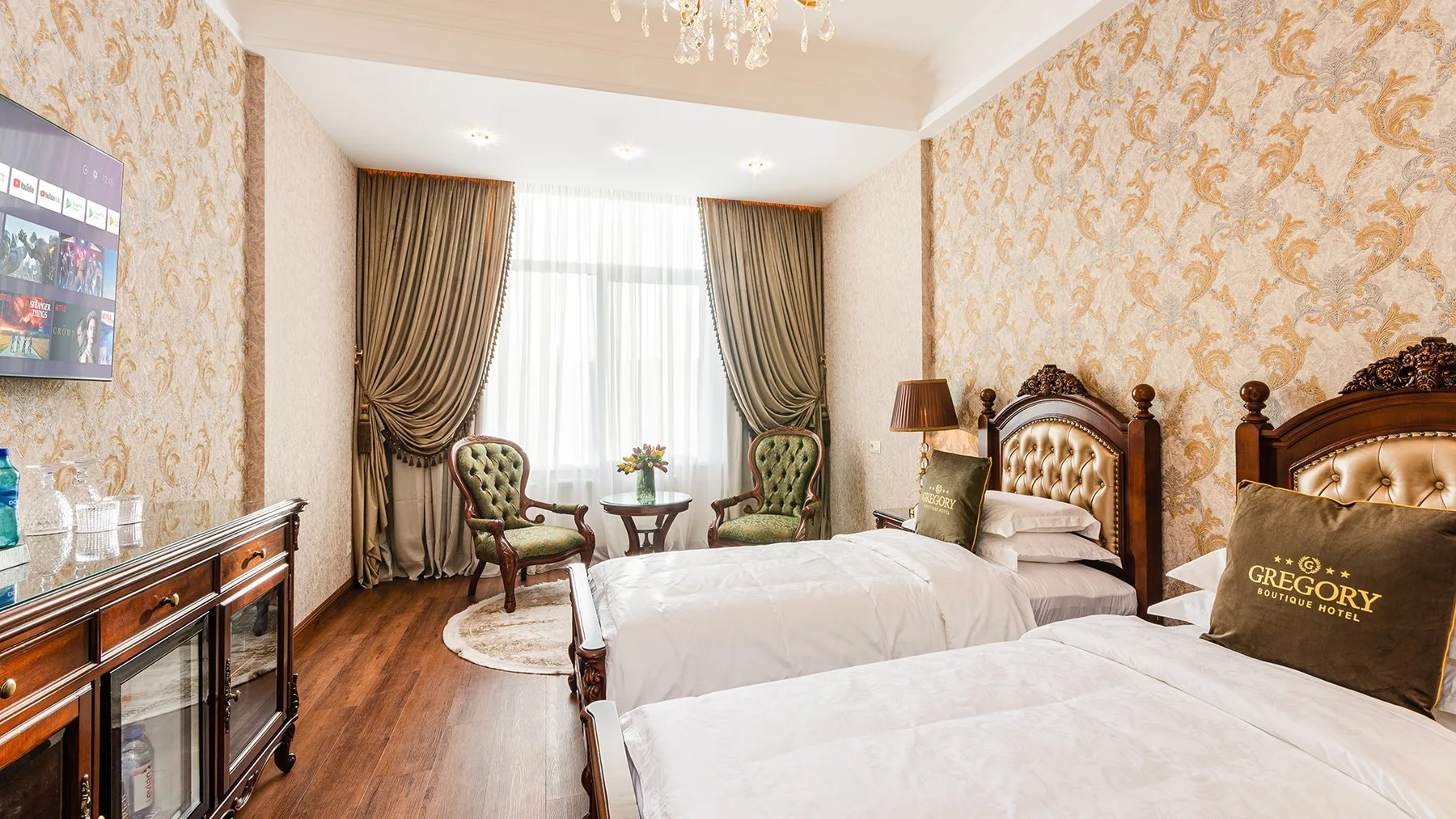 Representative hotel space: A bedroom with two beds, patterned wallpaper, and a seating area by the window.