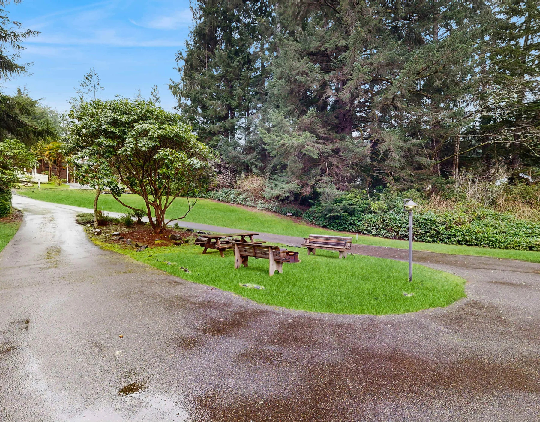 Una zona de picnic al aire libre con asientos de madera junto a un sendero pavimentado y césped verde.