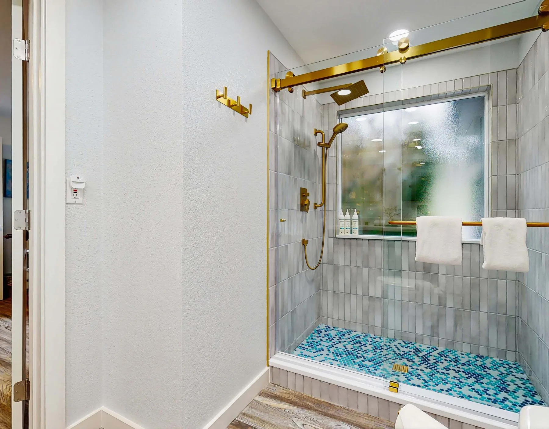 Una ducha revestida de azulejos, con panel de vidrio y piso de mosaico azul.