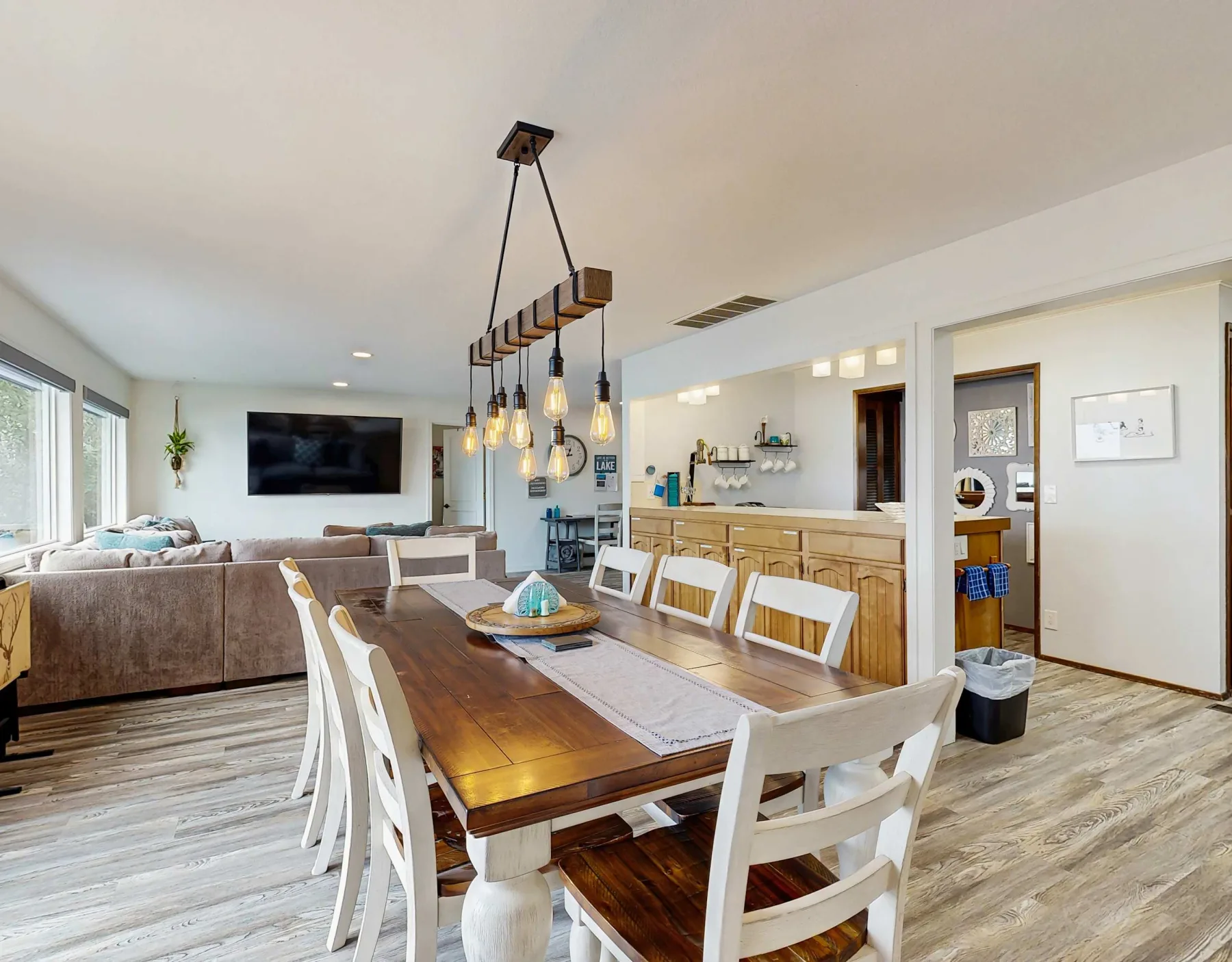 Espacio abierto de comedor y sala con una mesa de madera y asientos blancos.
