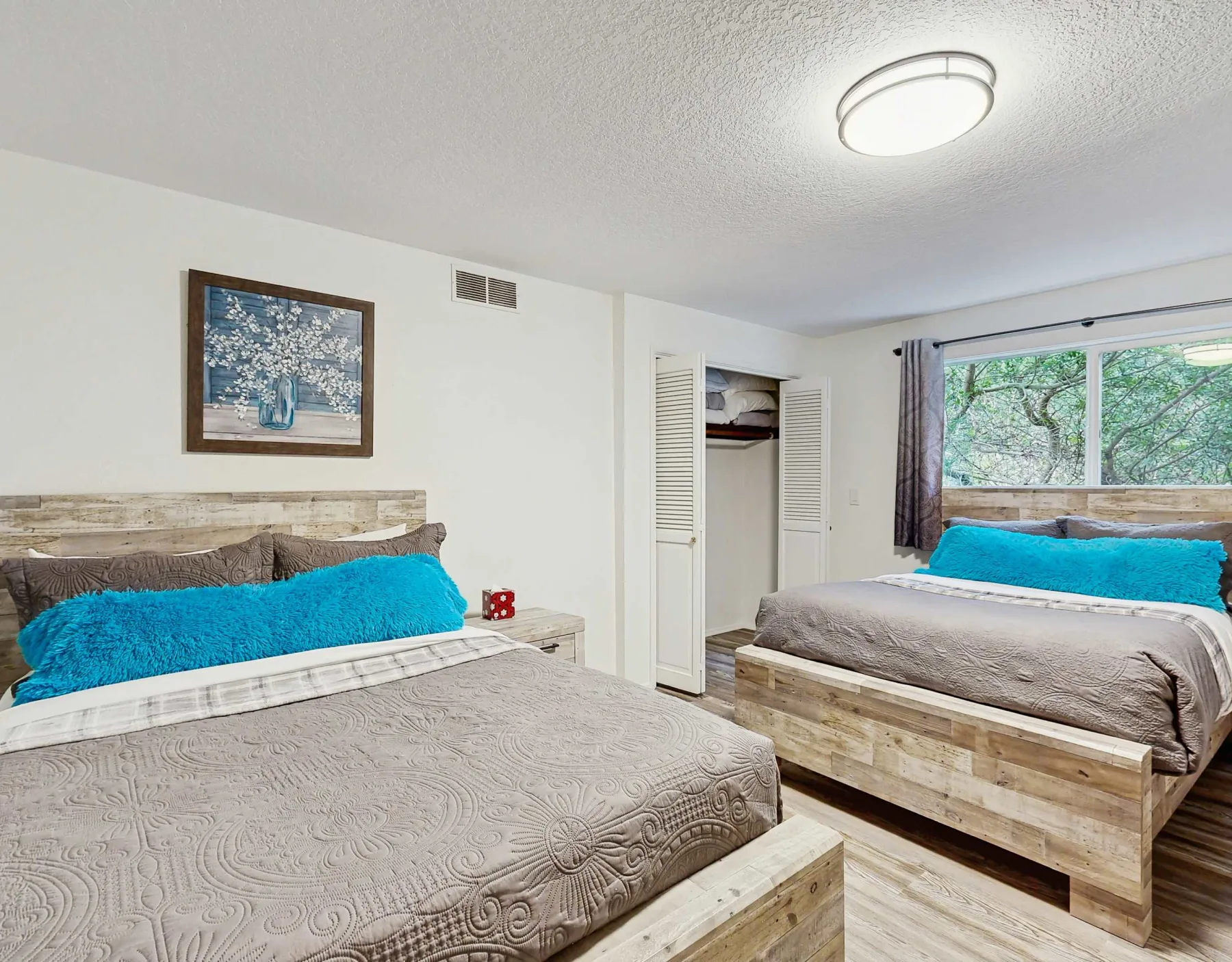 Un dormitorio con dos camas, almohadas turquesas y una ventana grande.