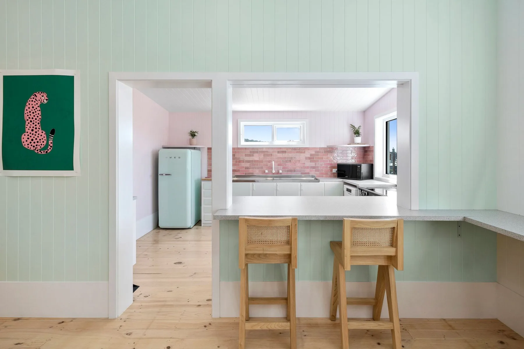 Una cocina luminosa con una barra, taburetes de madera y un salpicadero de azulejos rosas.