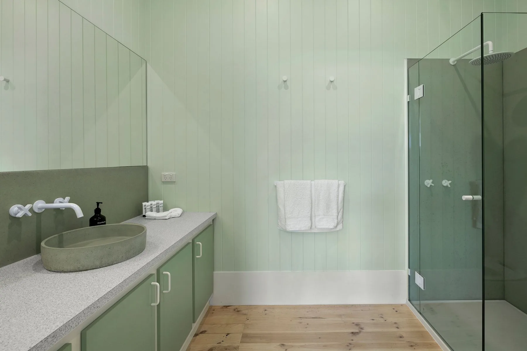 Un baño con un lavabo sobre la encimera, gabinetes verdes y una ducha de vidrio.
