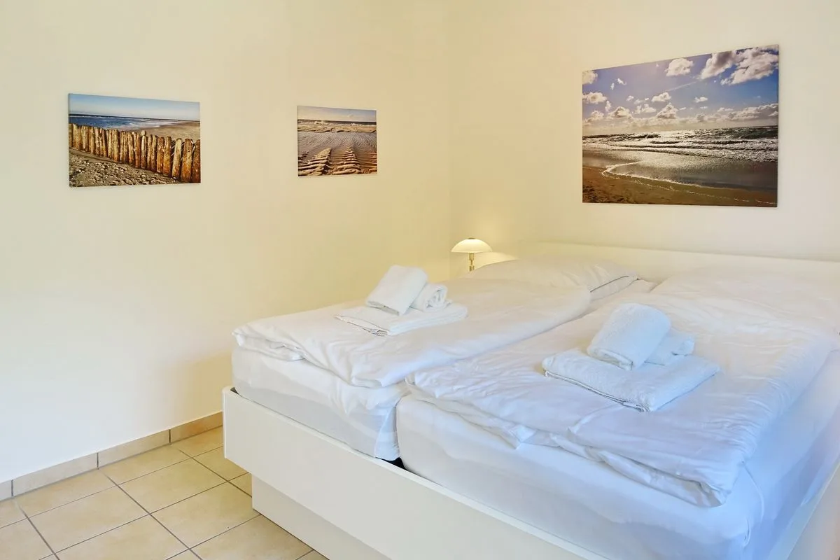 A bedroom with two beds dressed in white linens and coastal photographs on the wall.