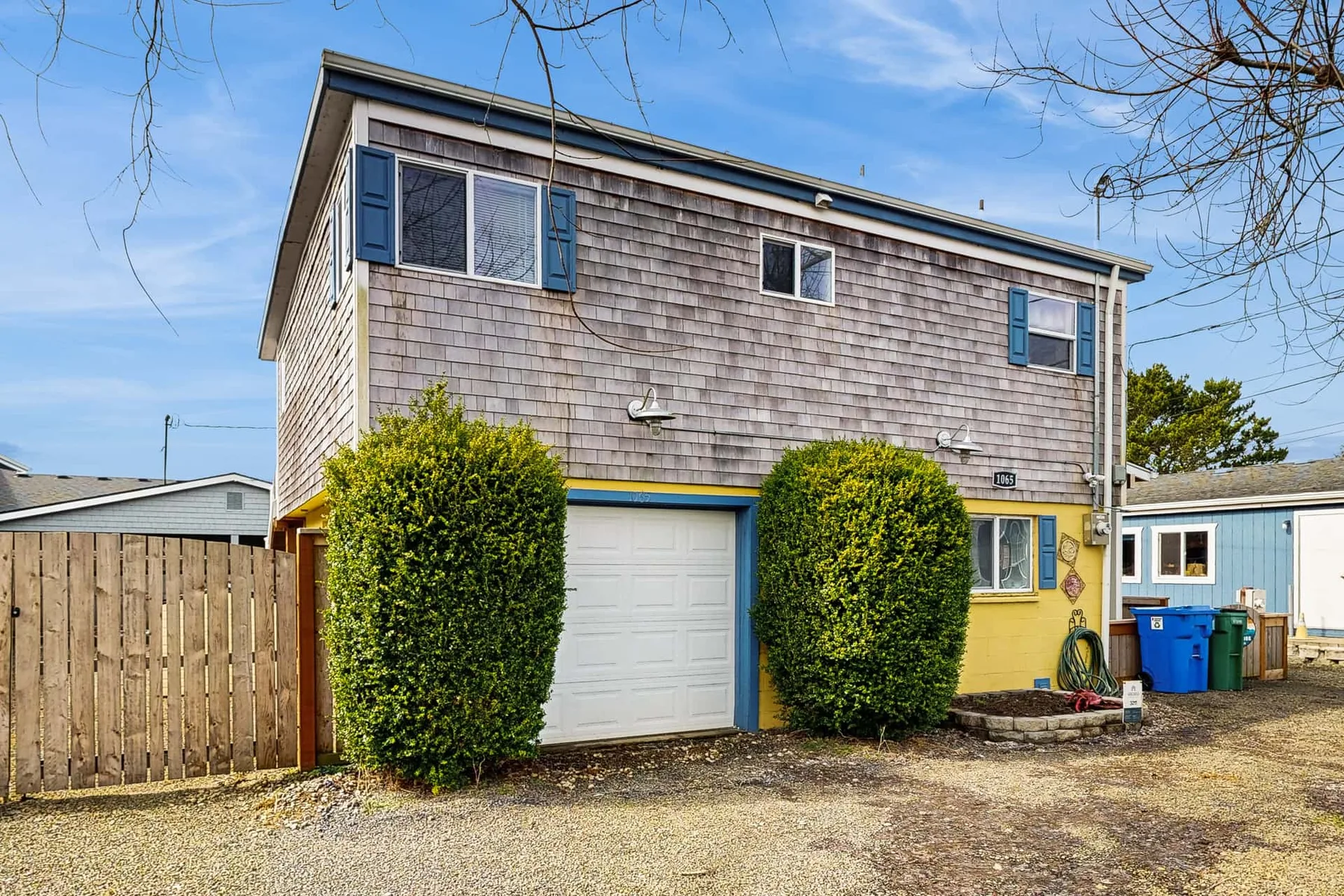 A two-story house exterior with shingle siding, a garage, and shrubs.