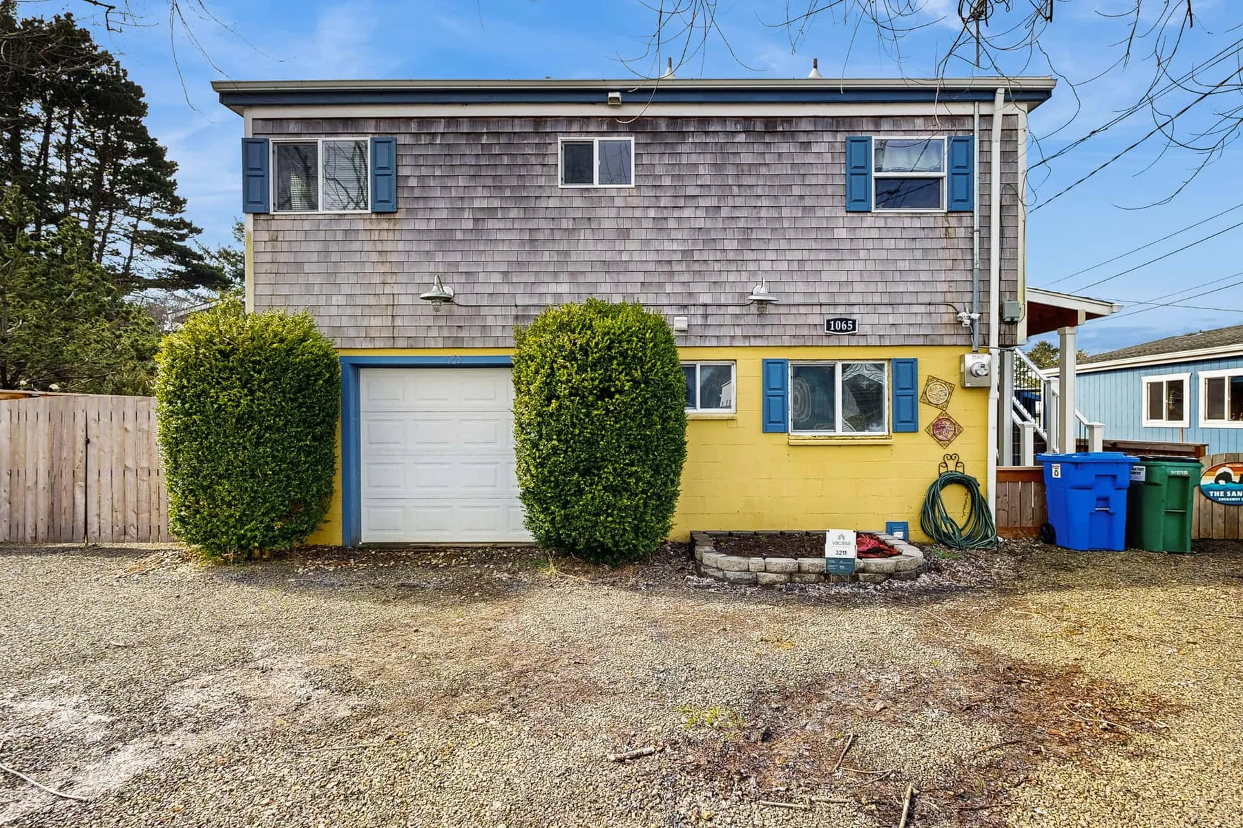 A two-story house exterior with gray shingles, yellow siding, and a garage door.