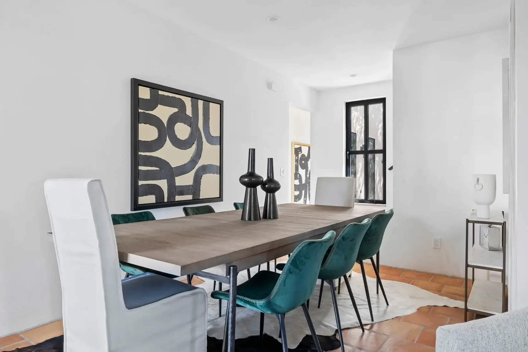A bright dining area with a long table, teal seating, and abstract wall art.