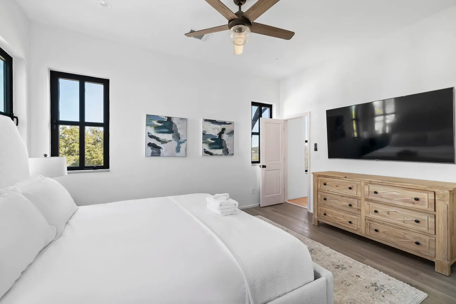 A bright bedroom with a neatly made bed, wall art, and a television on a dresser.