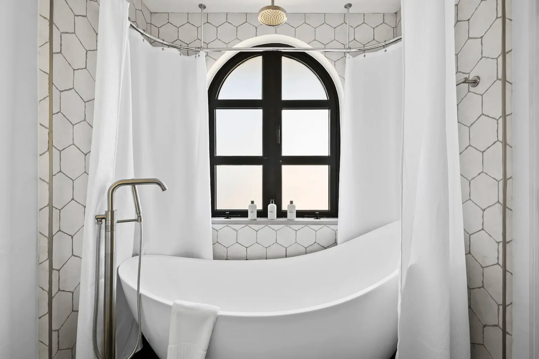 A bright bathroom features a freestanding bathtub beneath an arched window.
