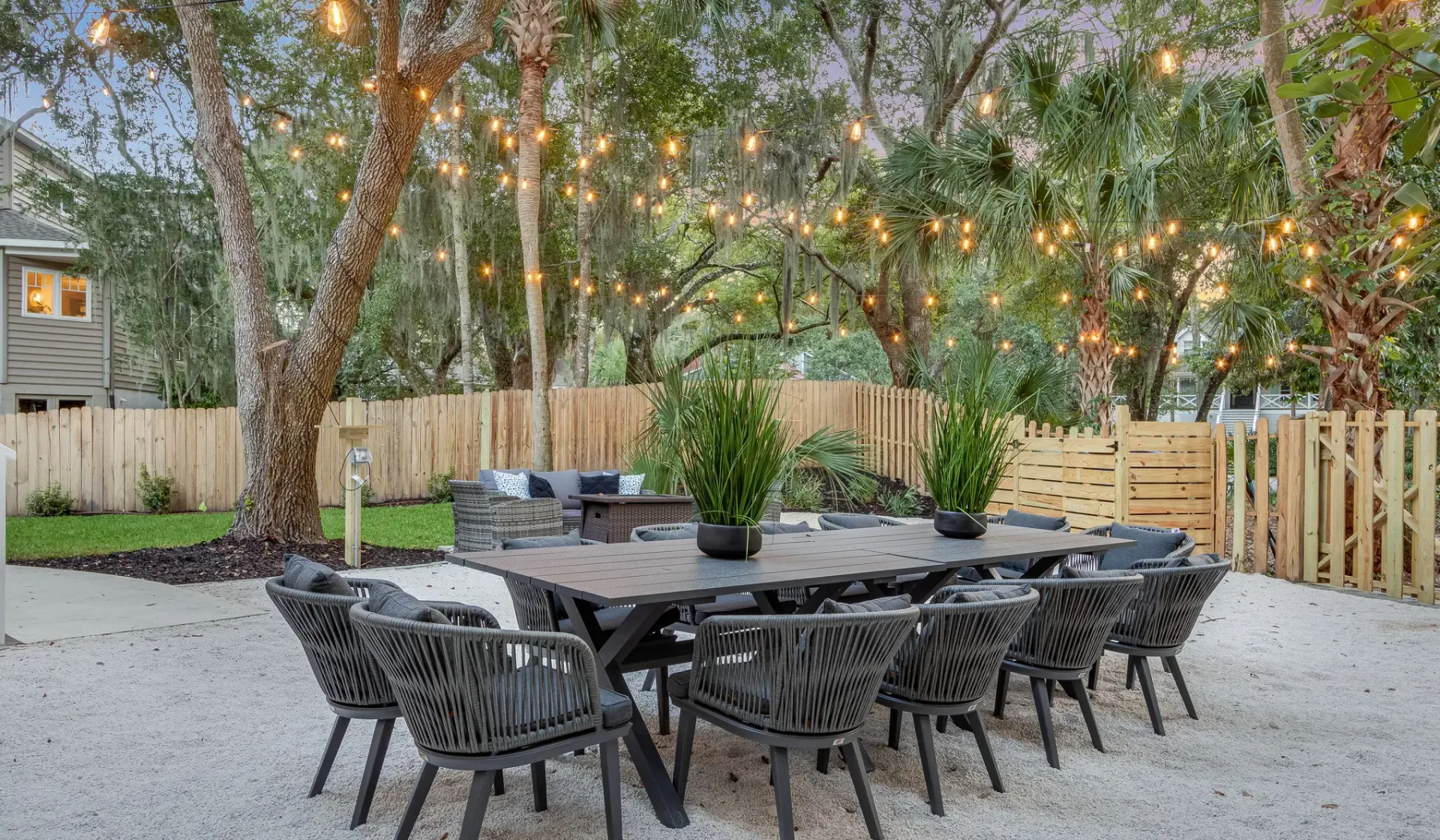 An outdoor dining area with a long table and string lights among the trees.